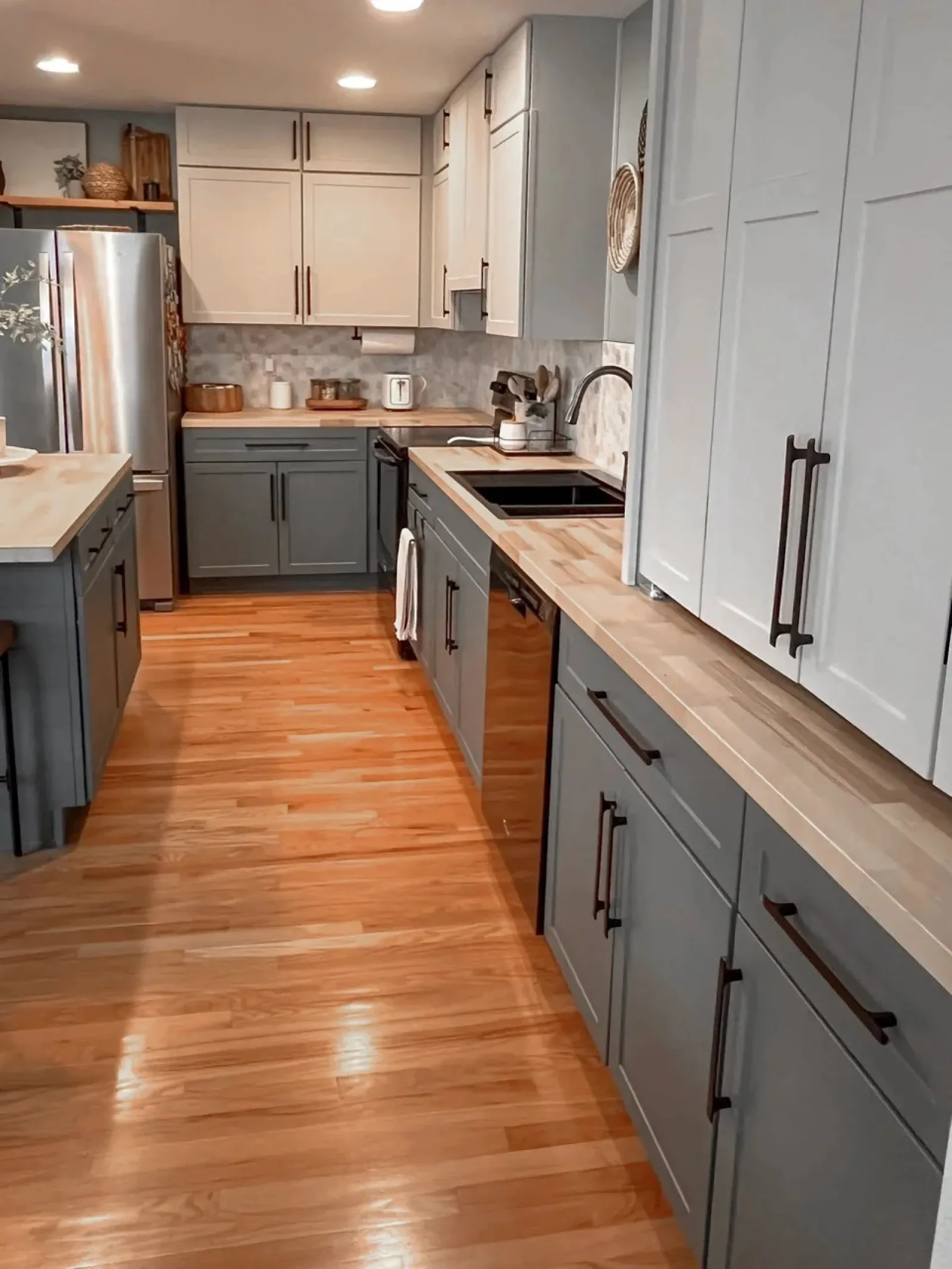 Modern kitchen with gray and white cabinets, wooden countertops, stainless steel appliances, and hardwood floors.