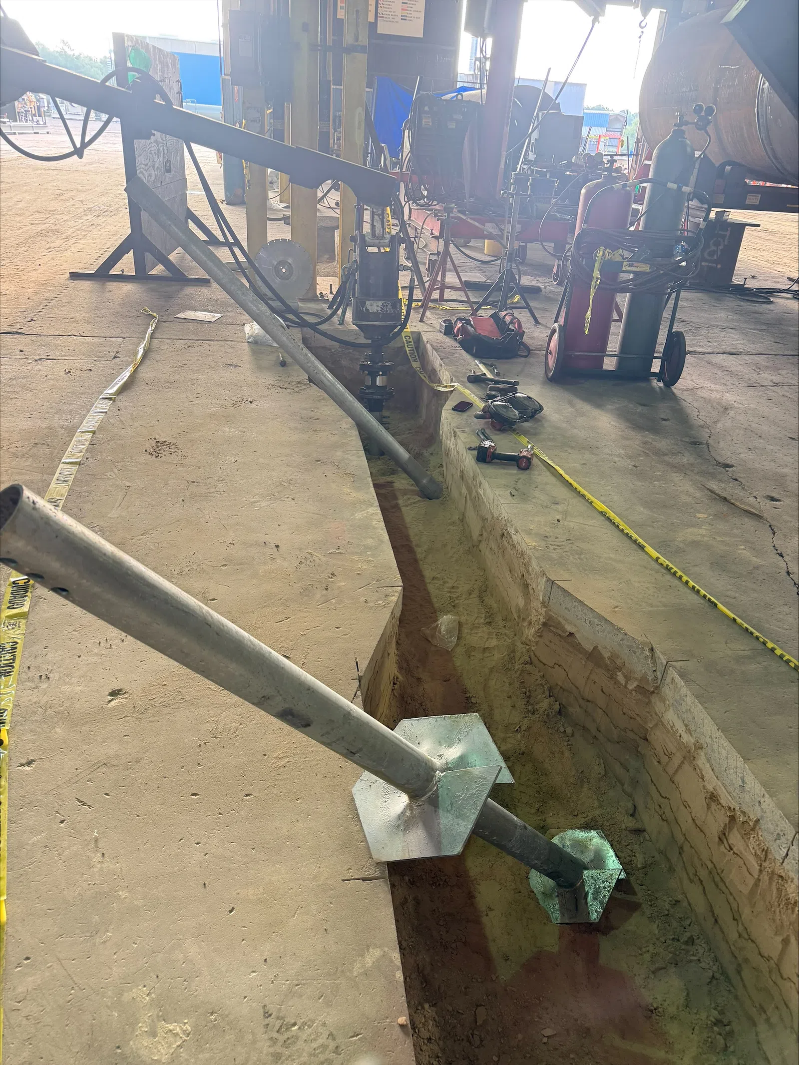 Construction site with metal anchors installed in a trench inside a workshop with tools and gas cylinders.