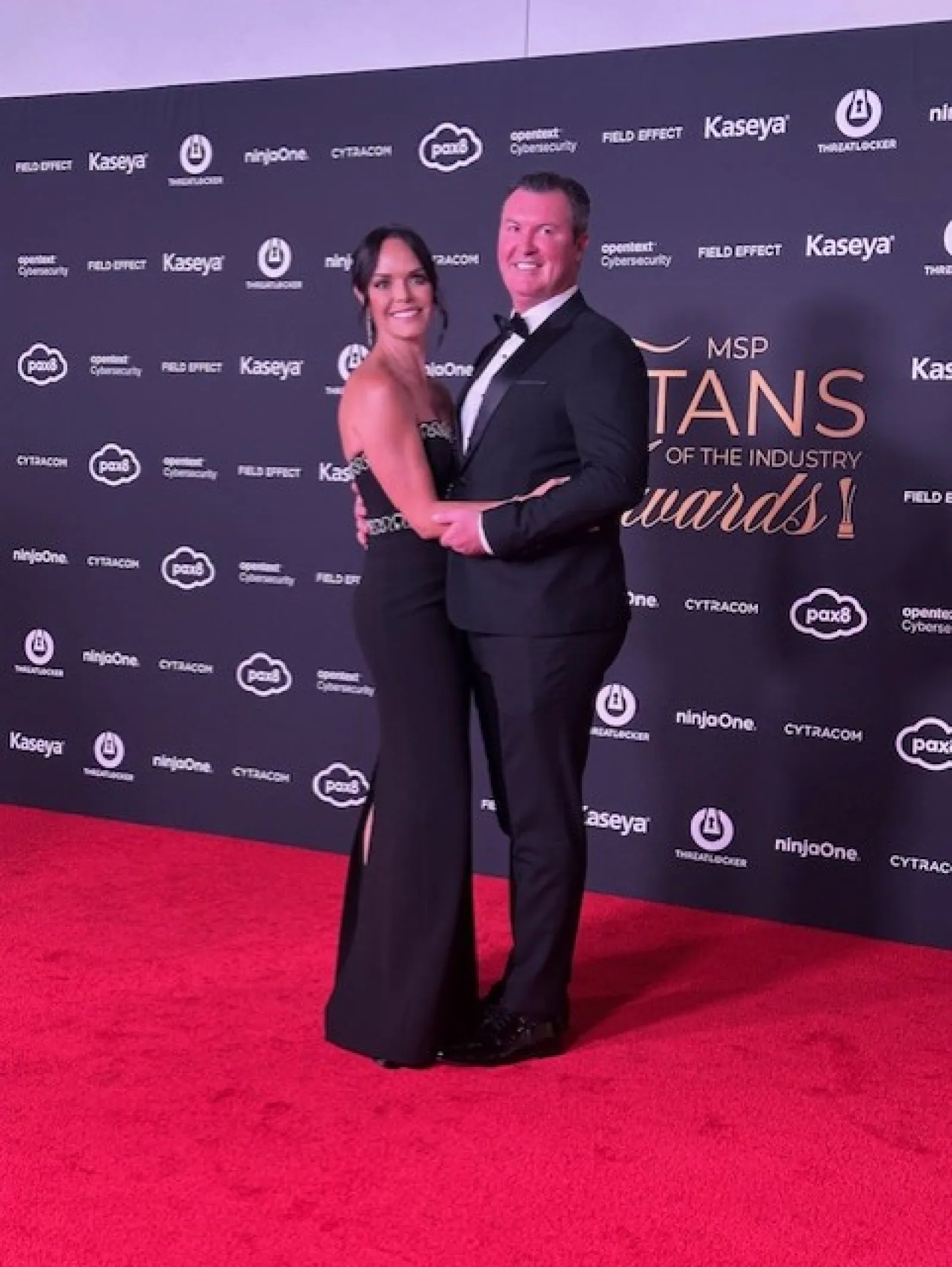 Couple in formal attire posing on a red carpet at MSP Titans of the Industry Awards event backdrop.