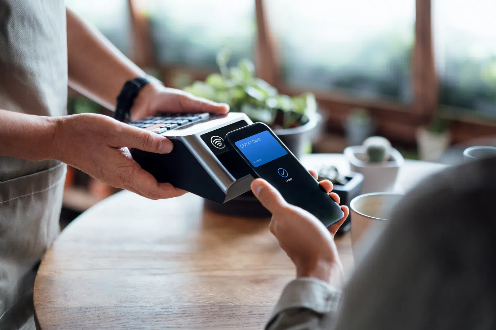 Customer making a contactless payment with a smartphone at a cafe using a card reader held by a barista.