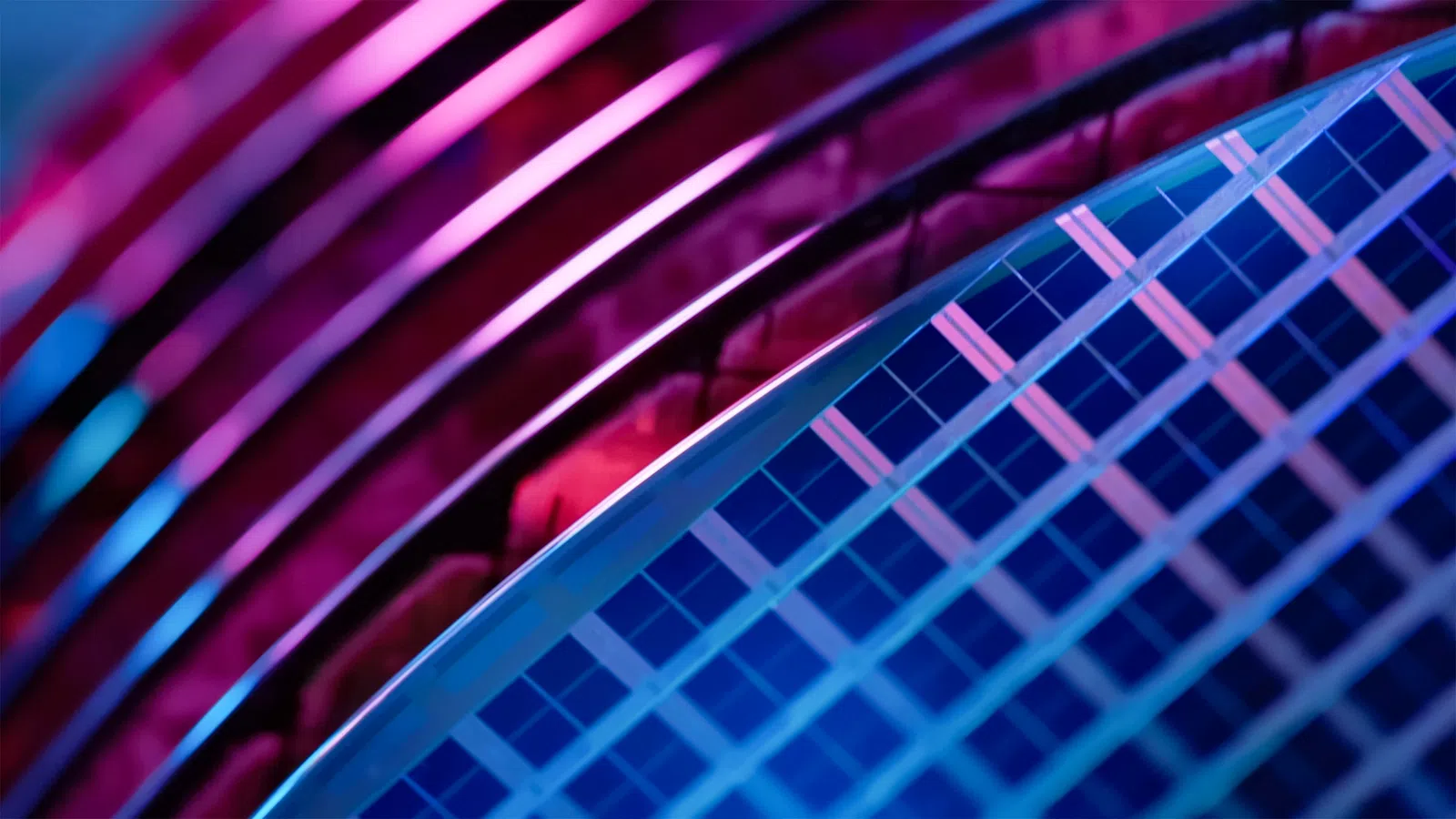 Close-up of a silicon wafer with grid patterns and curved reflective surfaces under purple and blue lighting.