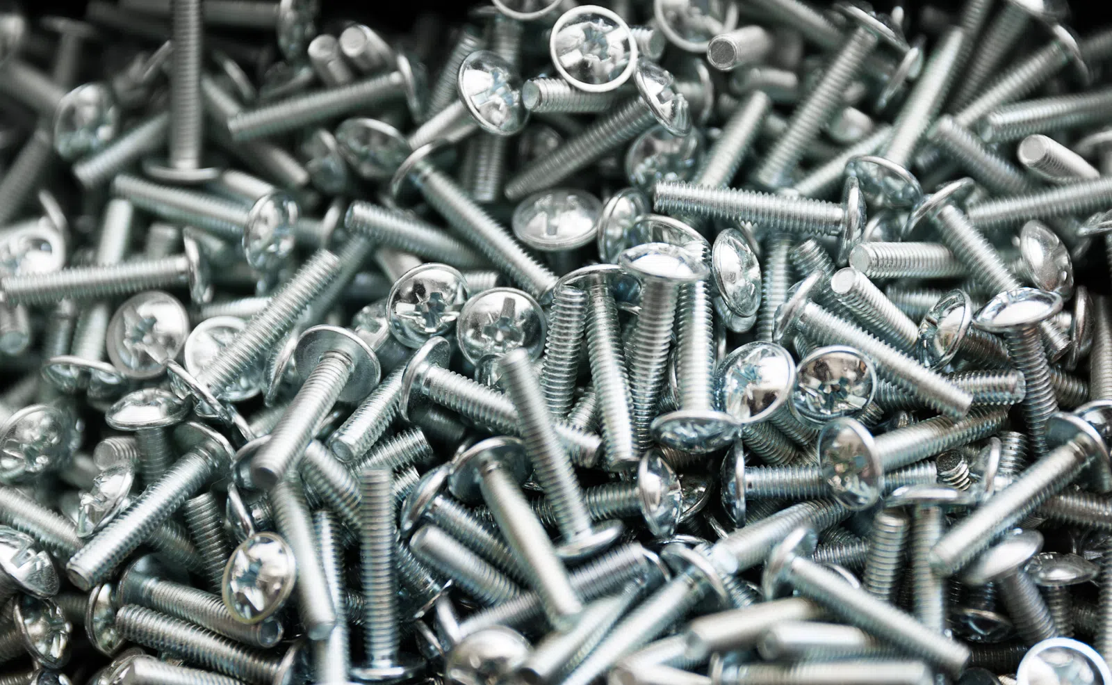 Close-up of shiny metal screws with Phillips heads piled together in a random arrangement.