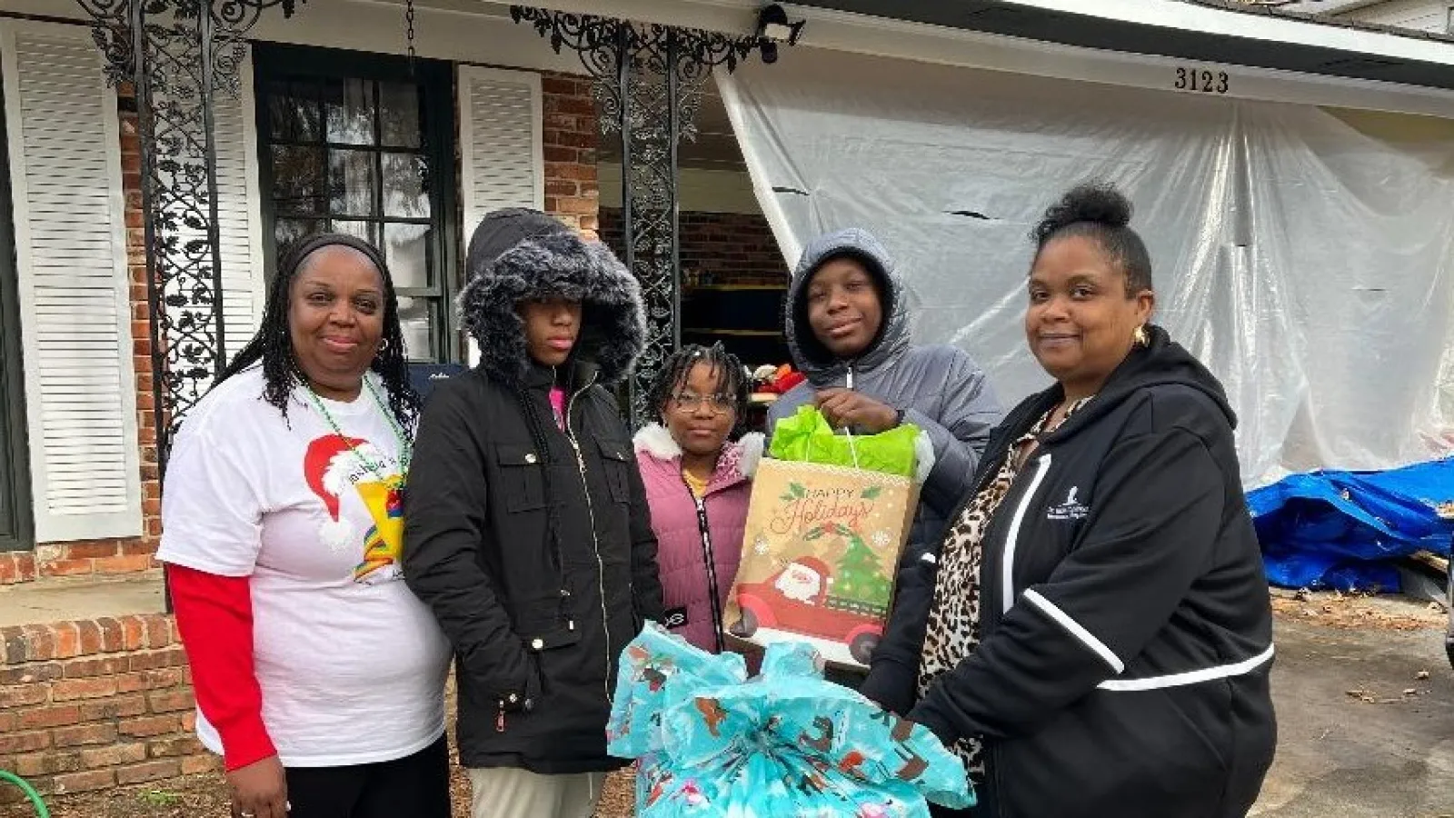 Group of five people standing outside a house with wrapped Christmas gifts and holiday bags