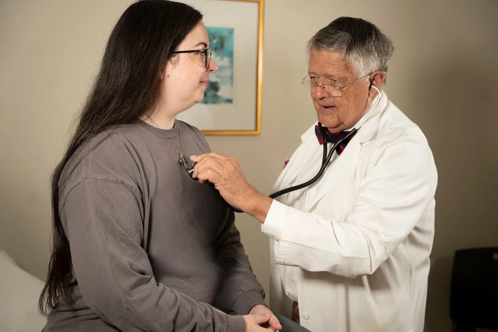 Doctor uses stethoscope to listen to patient's heartbeat during a medical checkup in an exam room.