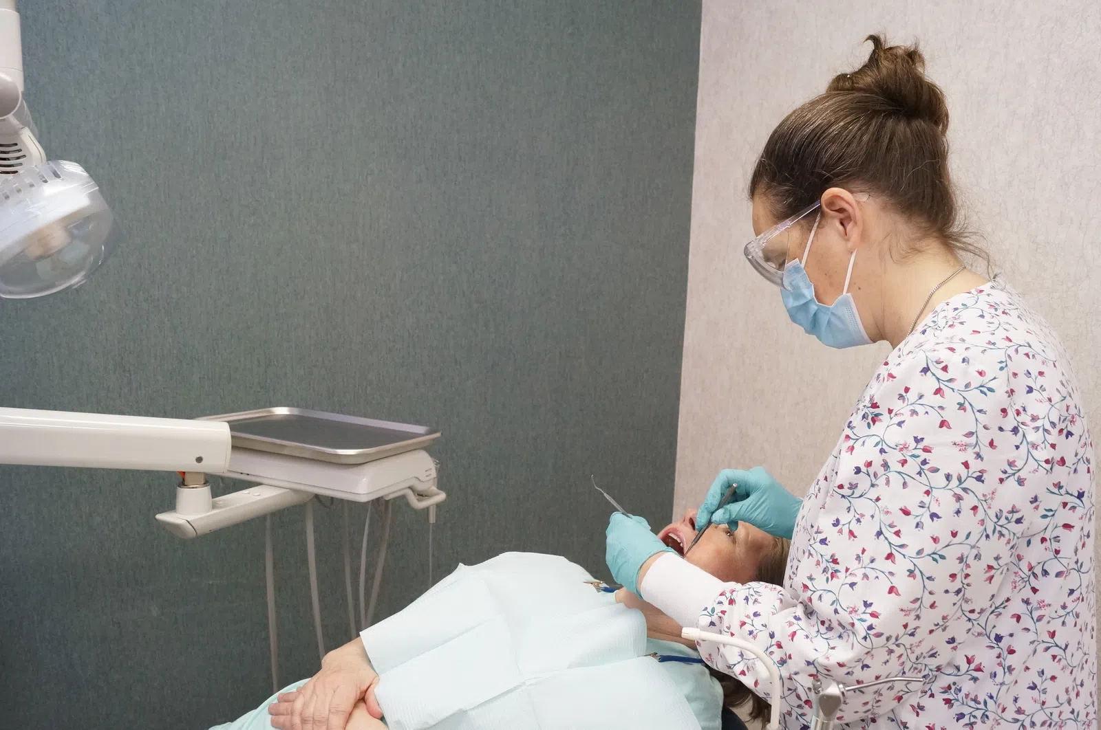 Dentist wearing mask and gloves examining patient lying on dental chair in clinic.