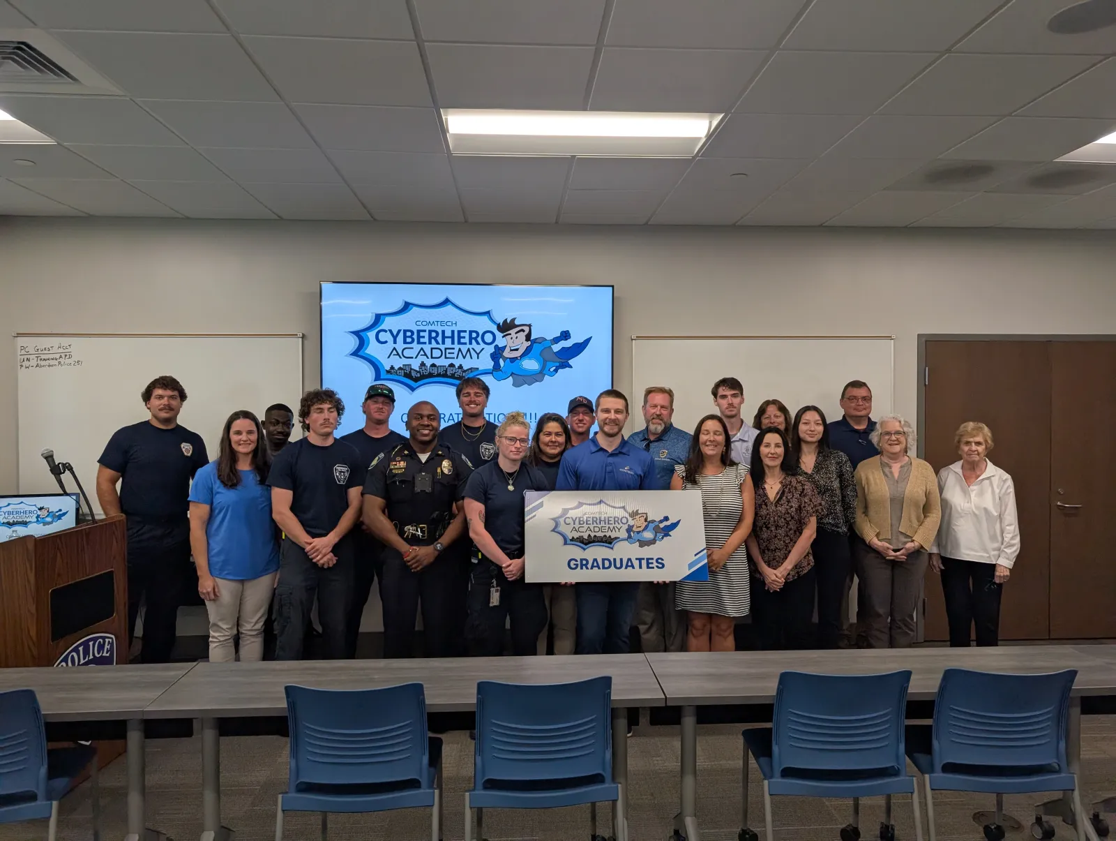 Group of graduates and instructors posing with CyberHero Academy banner in a classroom setting with a police emblem.