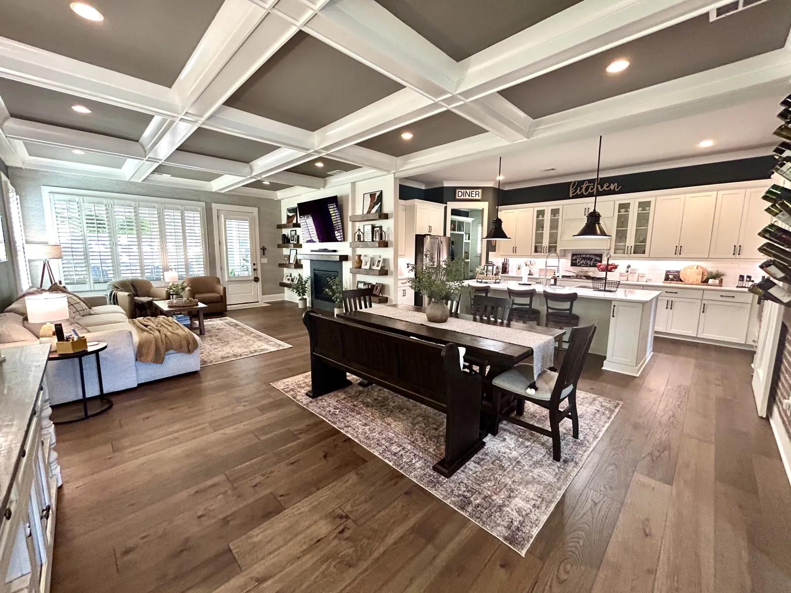 Spacious open living room and kitchen with coffered ceiling, hardwood floors, white cabinetry, and modern furniture.