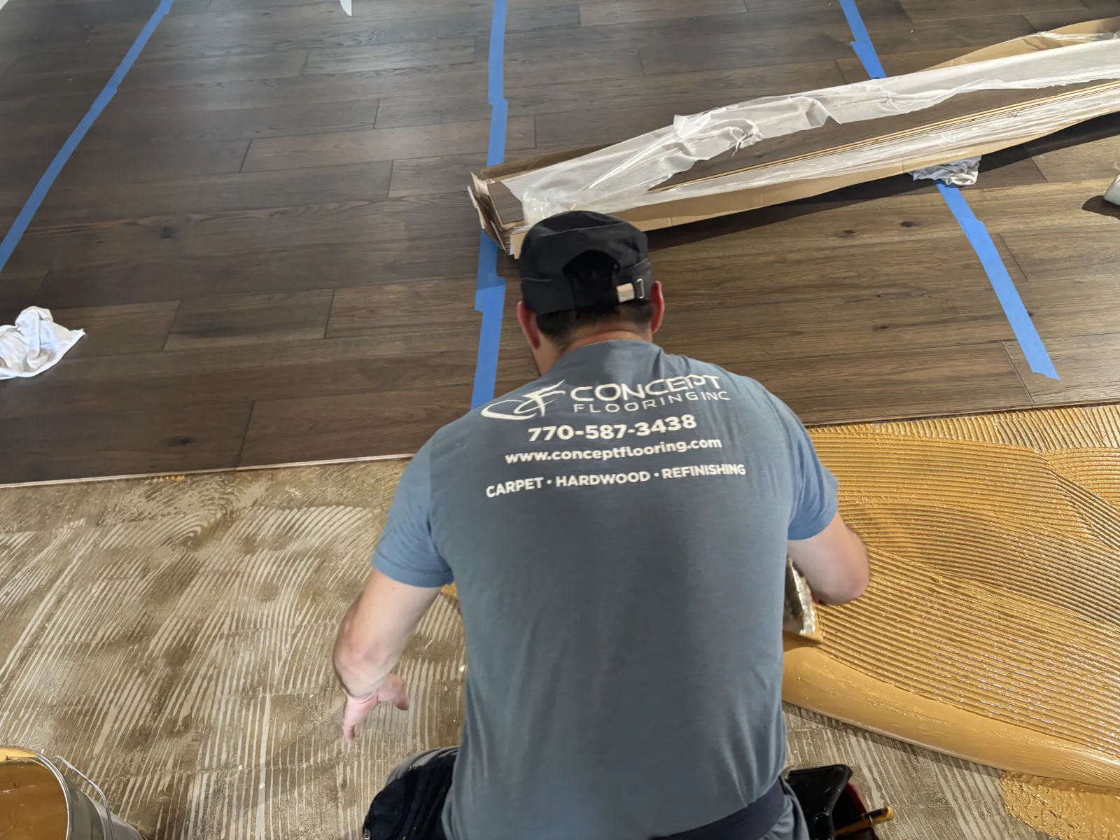 Flooring installer in Concept Flooring shirt spreading adhesive on floor preparing for hardwood installation.
