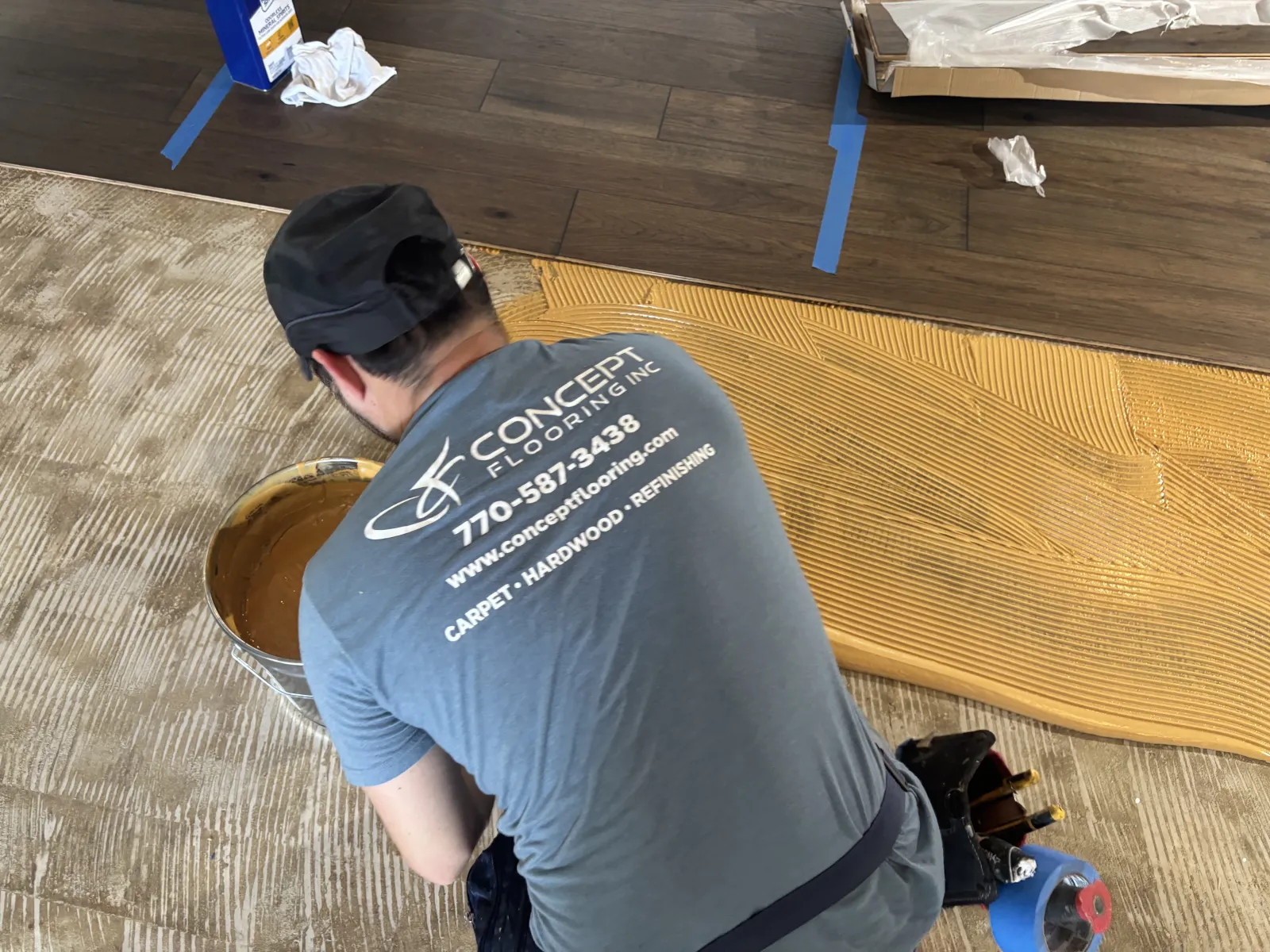 Professional flooring installer spreading adhesive on subfloor preparing for hardwood installation.