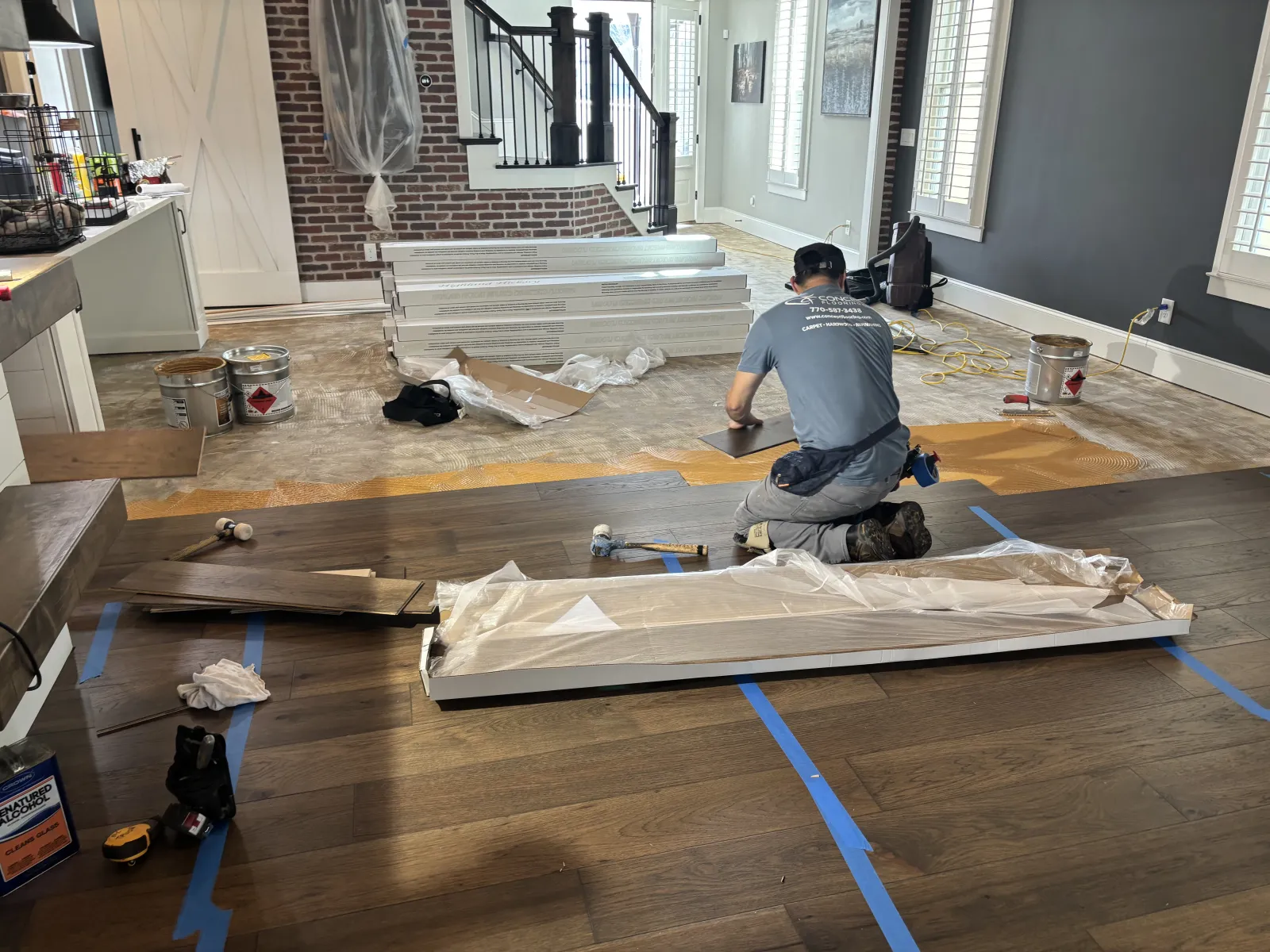 Worker installing hardwood flooring in a living room undergoing renovation with tools and materials scattered around.