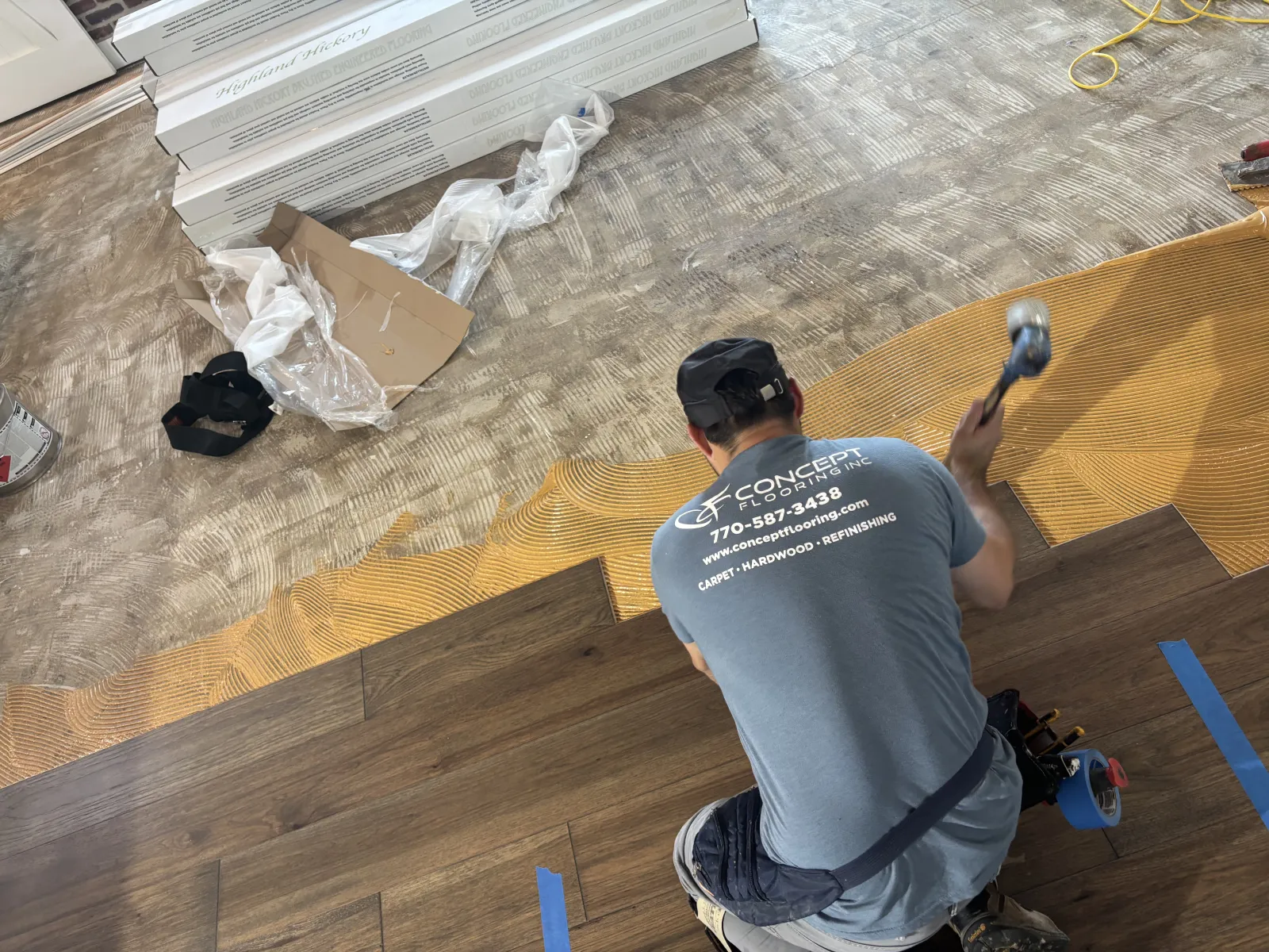 Worker installing dark wood laminate flooring over underlayment with tools in a room under renovation.