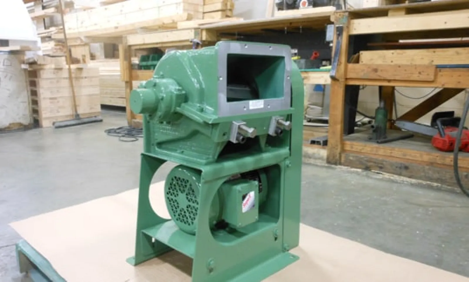 Green industrial machine with motor, mounted on a base in a workshop with wood and tools in the background