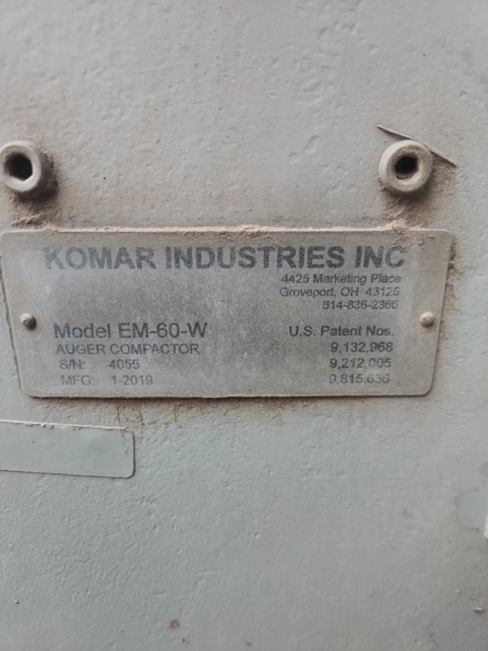 Metal identification plate of Komar Industries Inc auger compactor model EM-60-W with patent numbers and manufacturing date.
