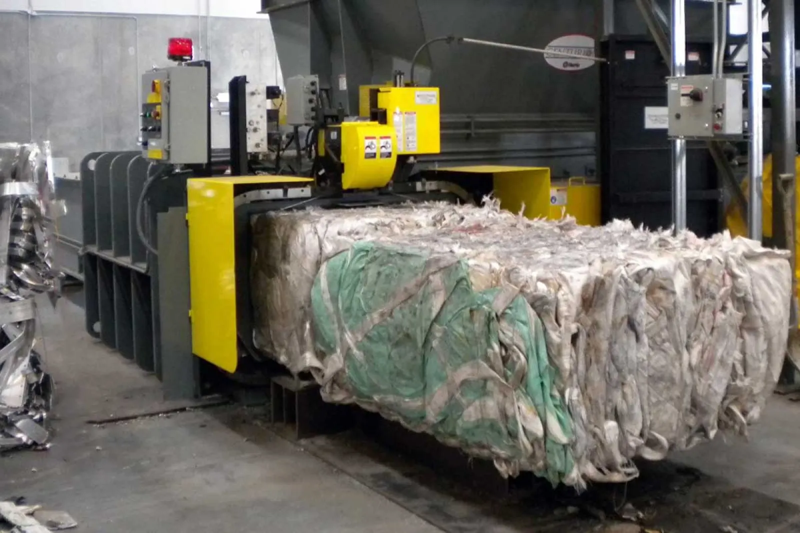 Industrial machine compressing large bales of fabric or plastic waste in a recycling facility.