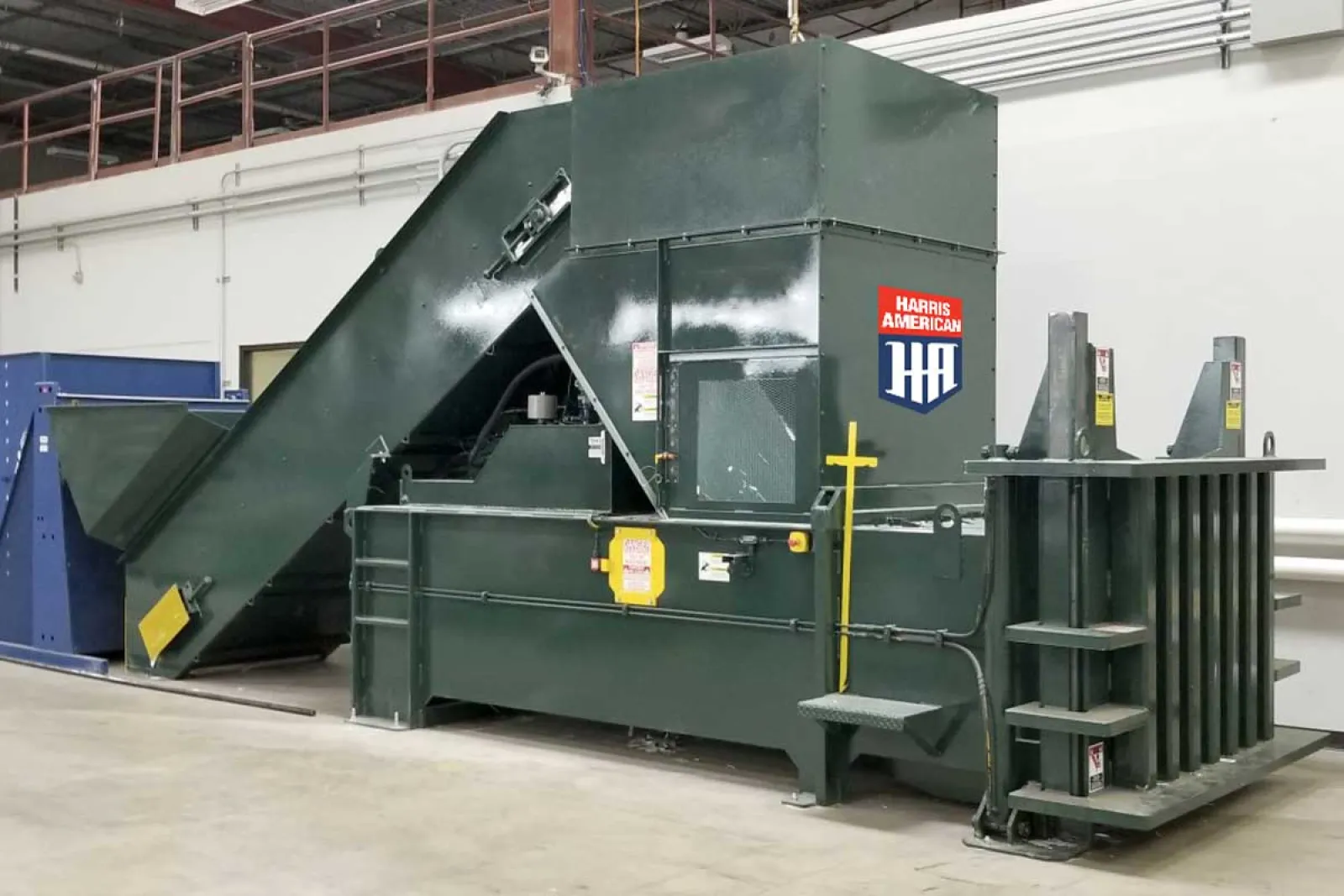 Large green industrial baler machine with Harris American logo inside a factory warehouse.