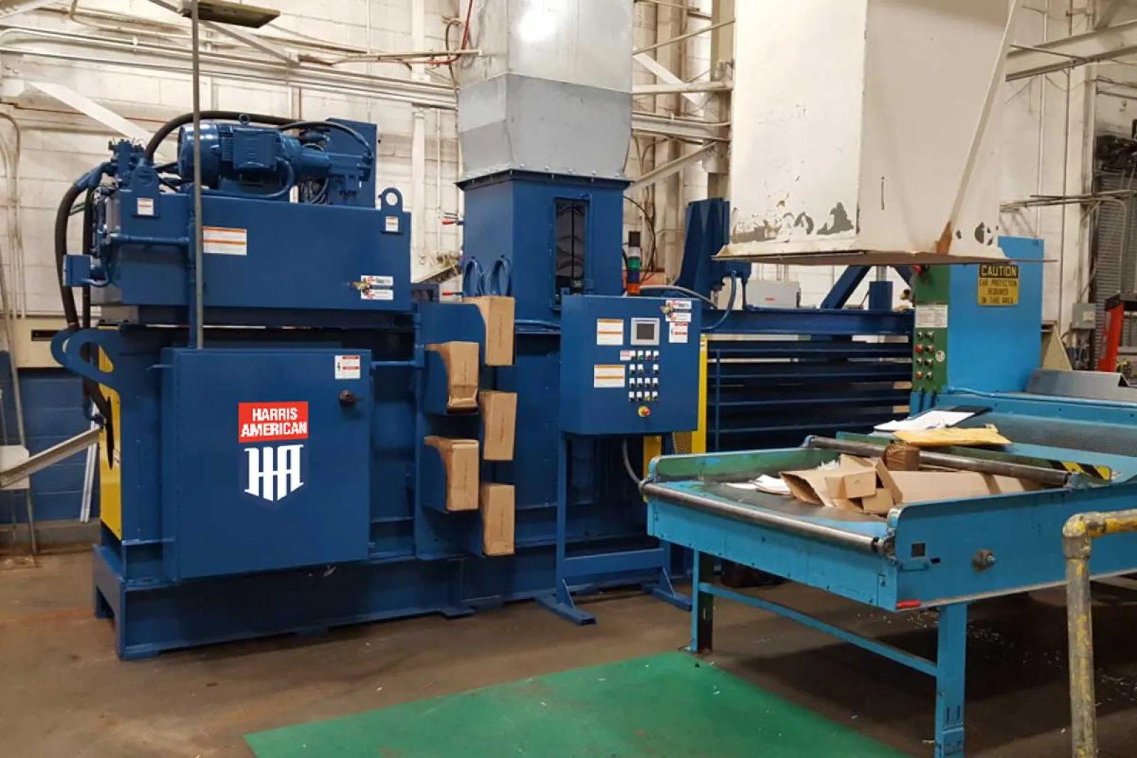 Industrial blue cardboard baler machine in factory setting with packed cardboard on conveyor belt.