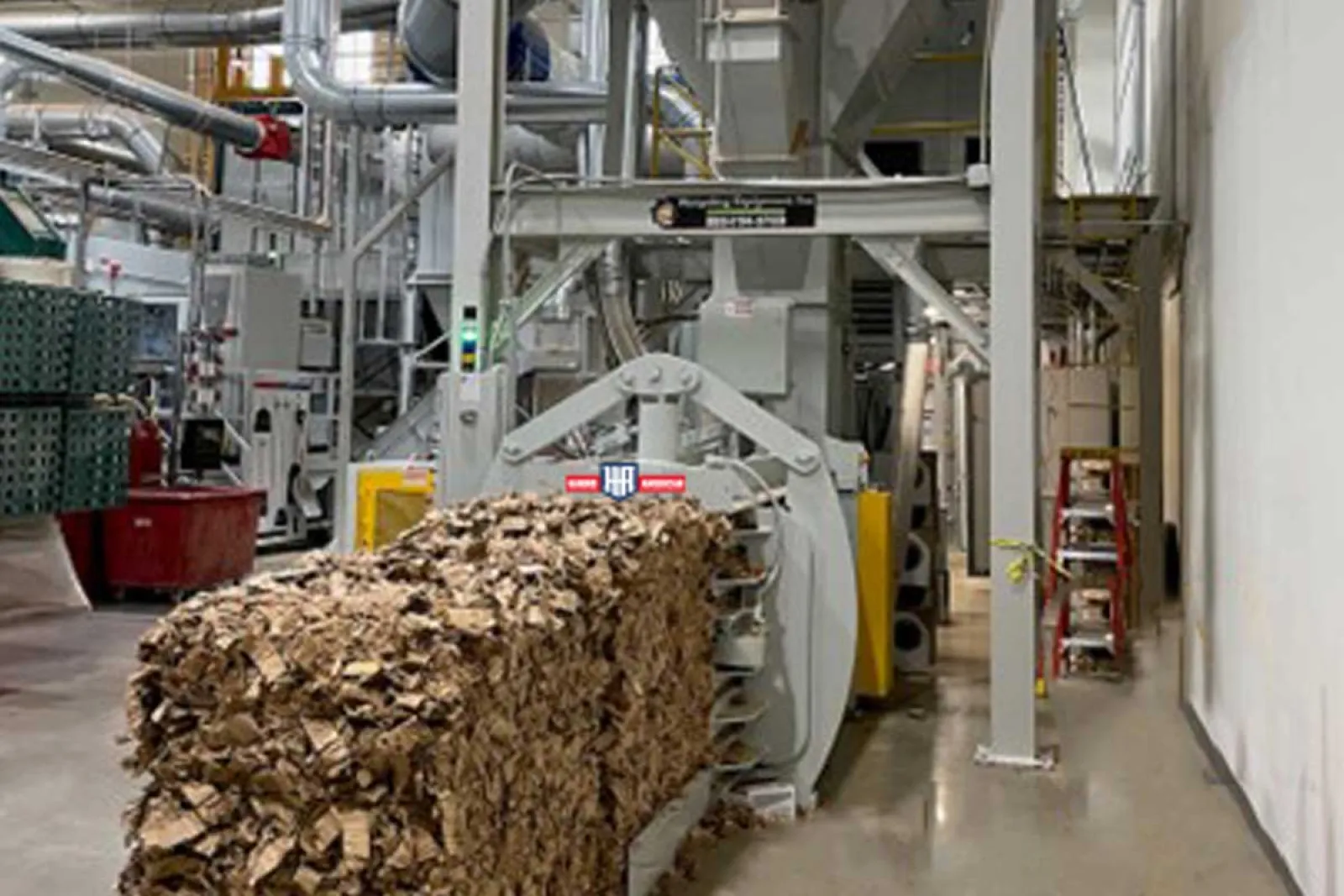 Industrial machine compressing large bales of brown cardboard in a recycling facility.
