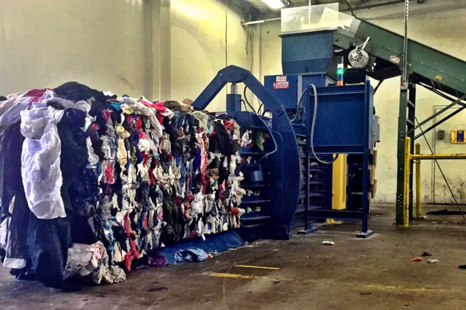 Industrial textile recycling facility with large compressed bales of mixed fabric and machinery in warehouse.