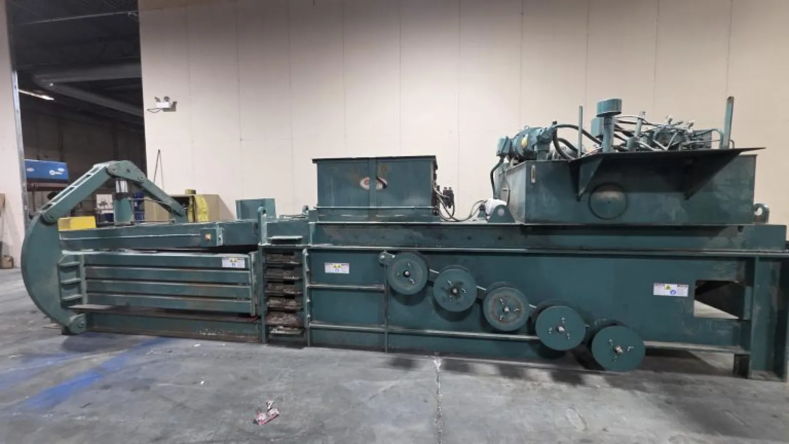 Large industrial green metal baler machine inside a warehouse on concrete floor, used for compacting materials.