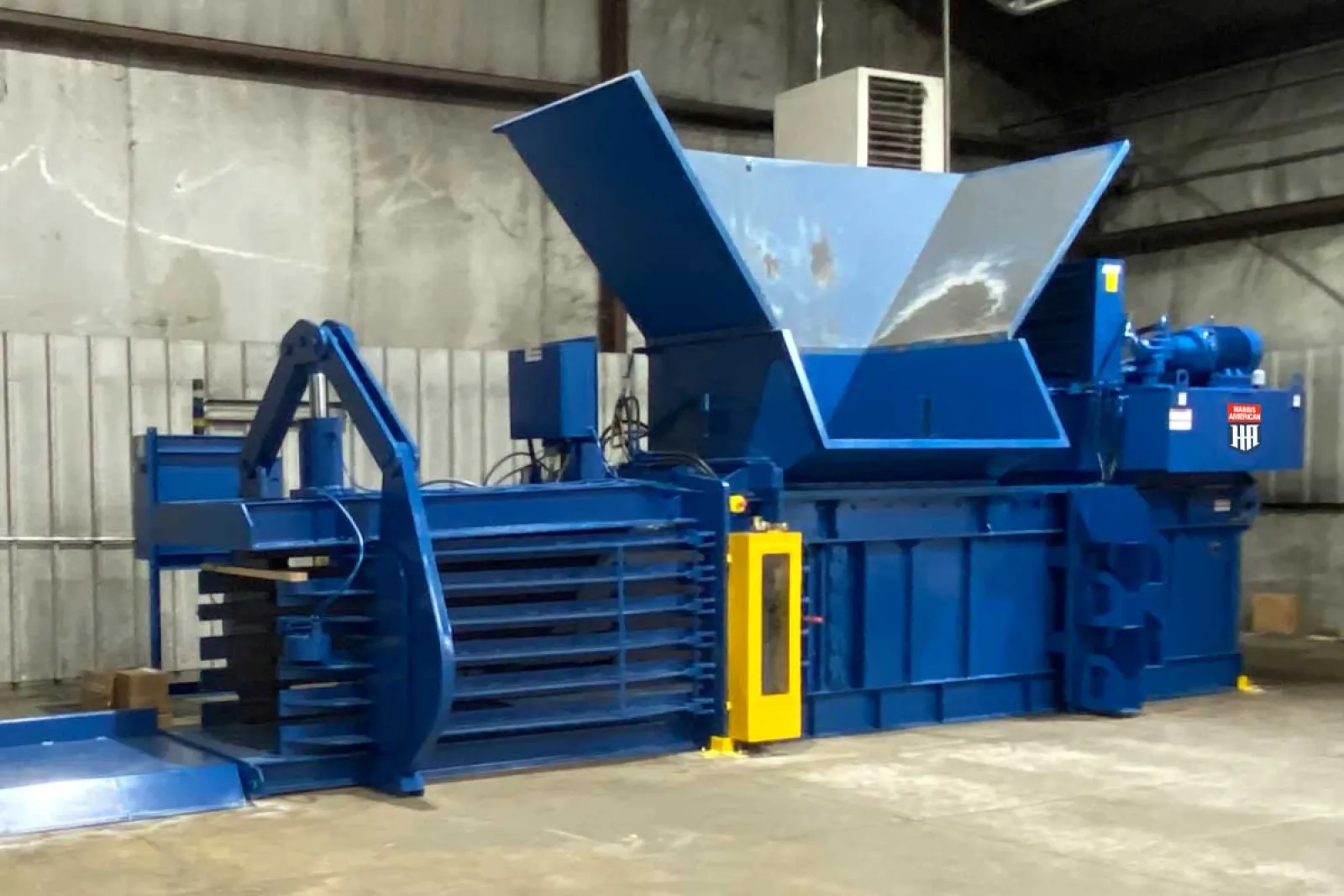 Large industrial blue baler machine with hopper in a warehouse environment