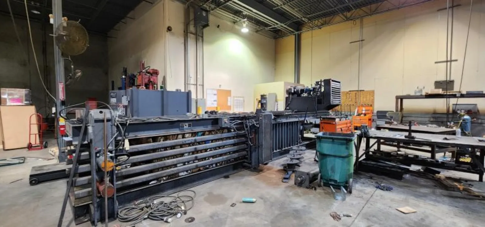 Industrial workshop with large machinery, metal tables, tools, and equipment under bright overhead lights.