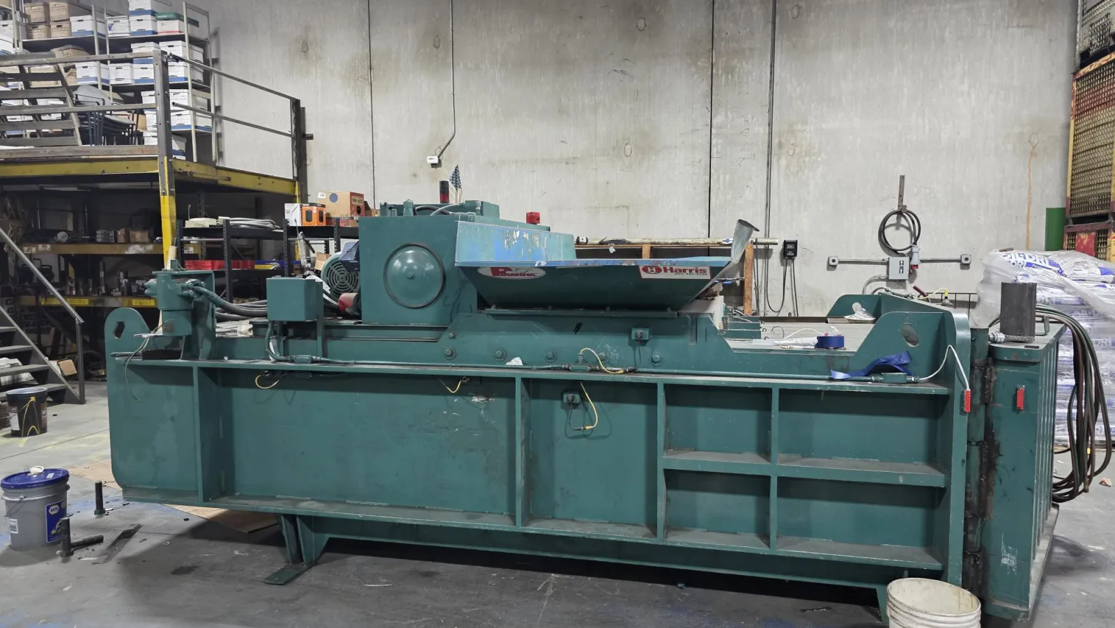 Industrial green machine with rotating mechanism in a warehouse with shelves and equipment.