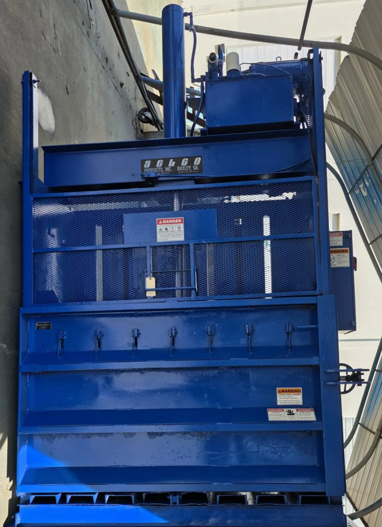 Large blue industrial Selco product machine with safety grills and warning labels in a sheltered outdoor area.