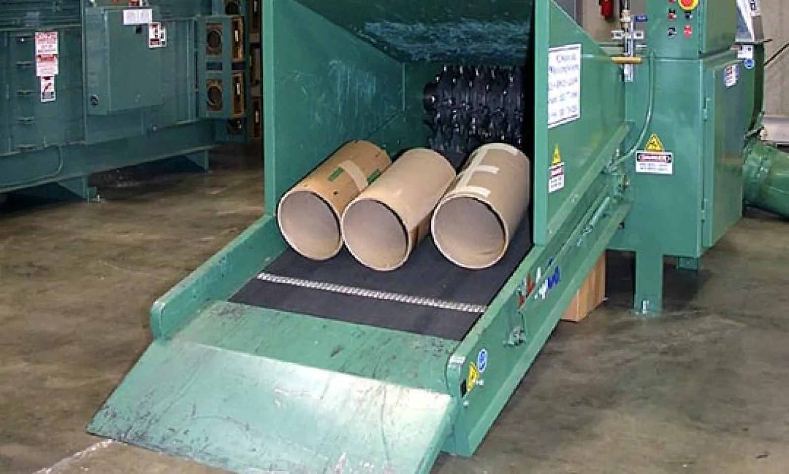 Industrial paper tube shredding machine processing large cardboard tubes on a factory floor conveyor belt.