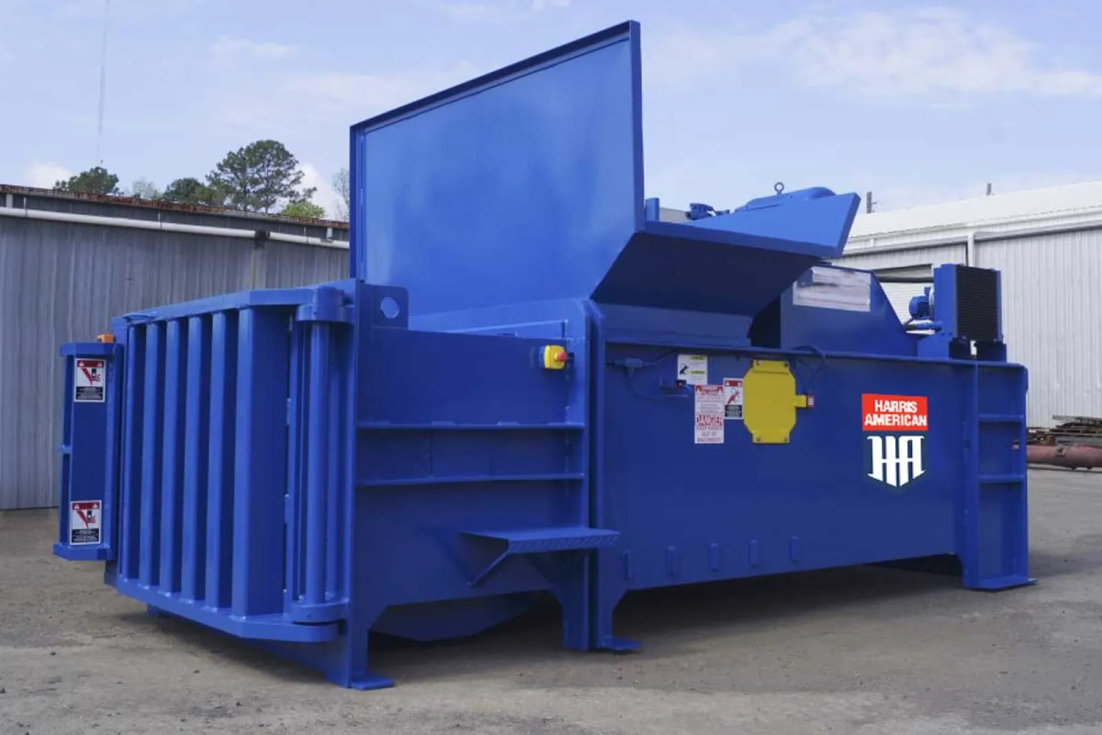 Large blue industrial trash compactor machine with open top and Harris American logo outdoors
