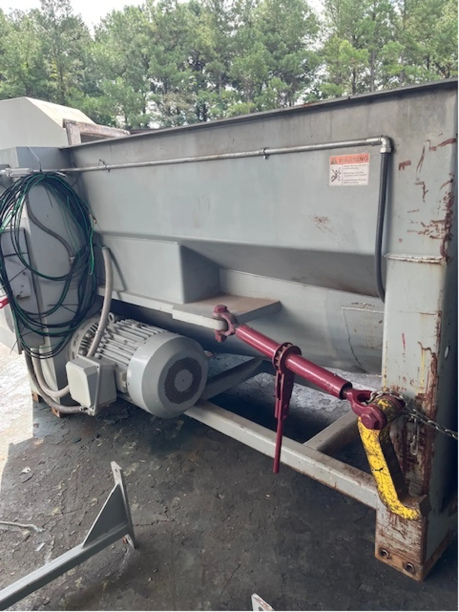 Large industrial machine with electric motor, coiled cables, and red-yellow mechanical handles on metal frame.