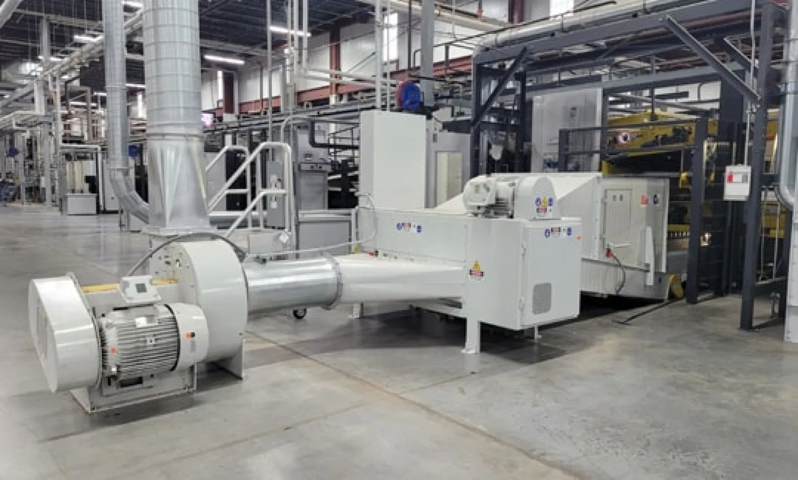 Large industrial machine with motor and ducting in a clean modern factory setting.