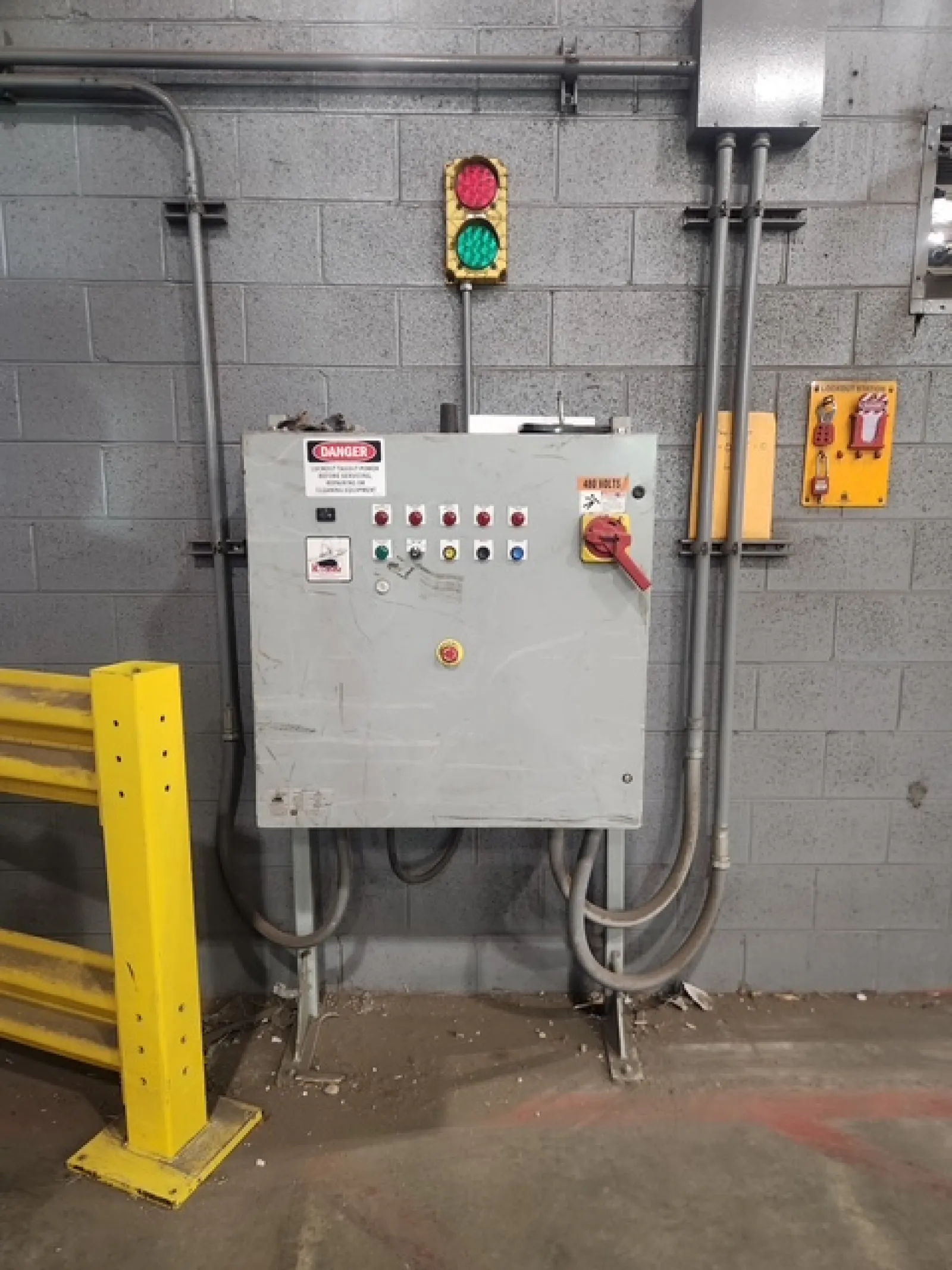 Industrial electrical control panel with safety warning signs and a traffic light mounted on a concrete wall.