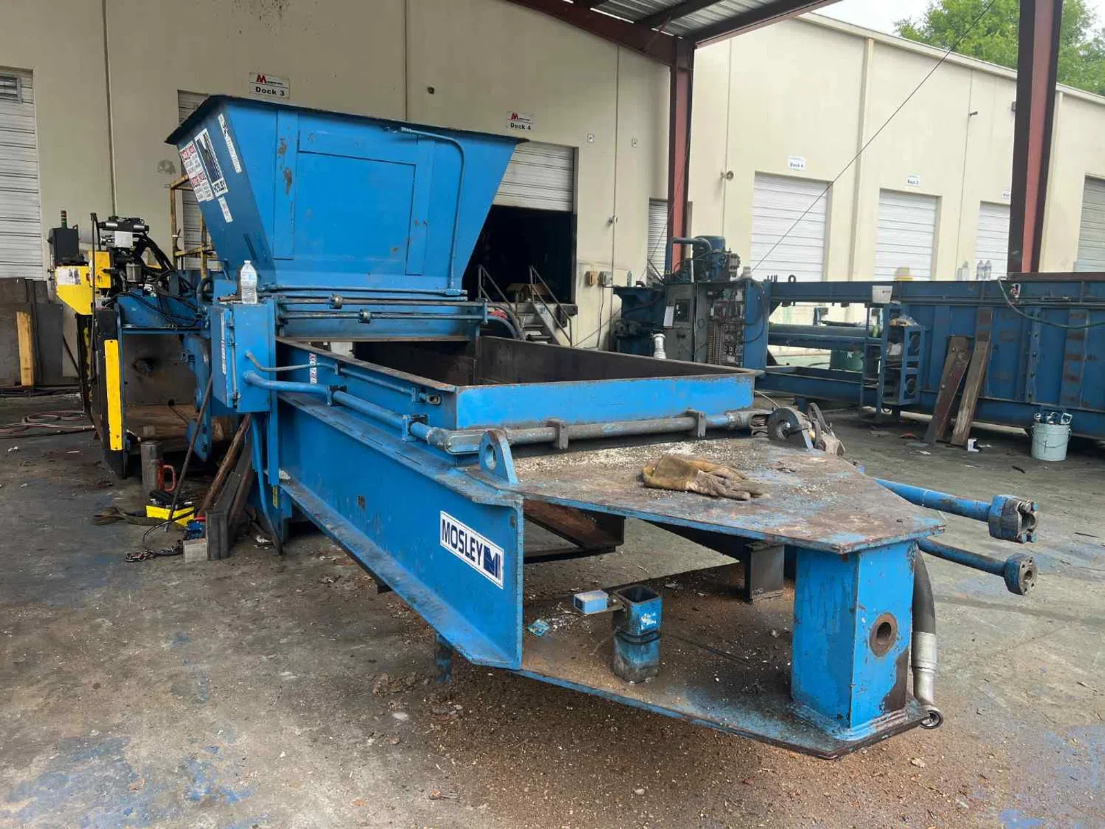 Blue Mosley industrial metal baler machine in a warehouse with open hopper and conveyor.