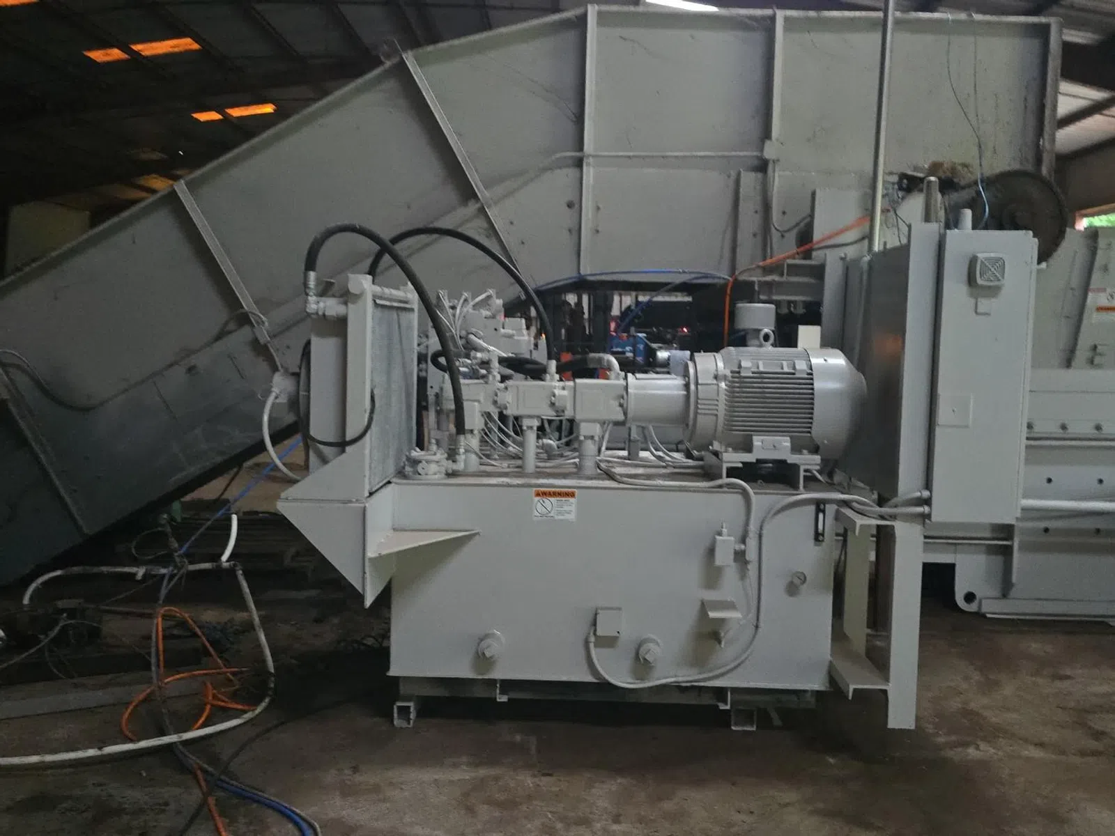 Industrial hydraulic power unit with motor, hoses, and control components in factory setting.