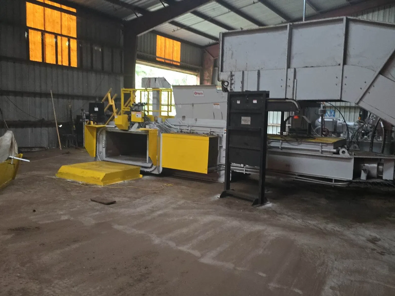 Industrial machinery with yellow panels inside a large factory with high ceilings and orange windows.