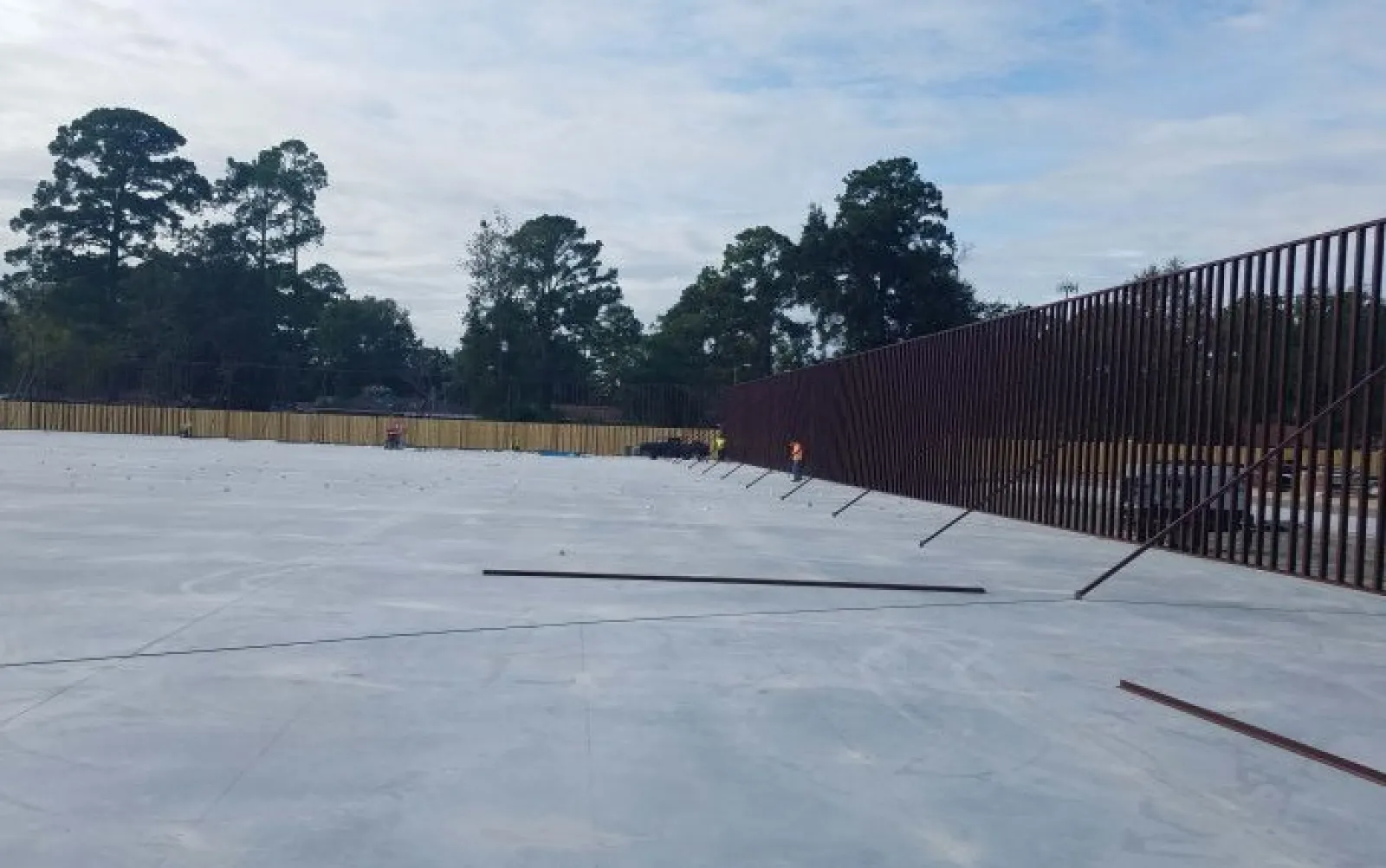 Large concrete slab with a tall metal fence along one side and trees in the background under a cloudy sky