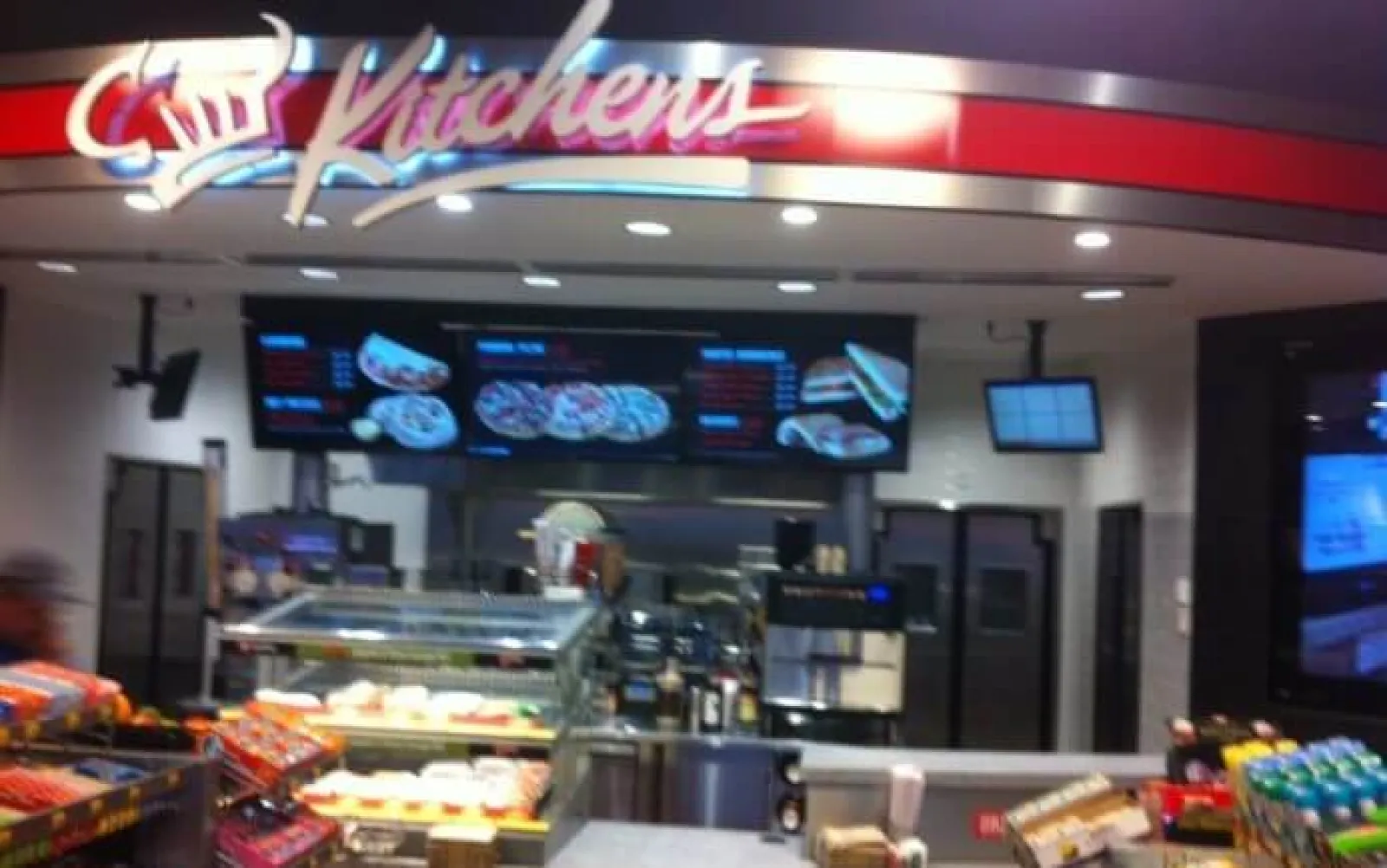 Interior of Kitchens fast food restaurant showing menu boards, counter, and food displays under red signage