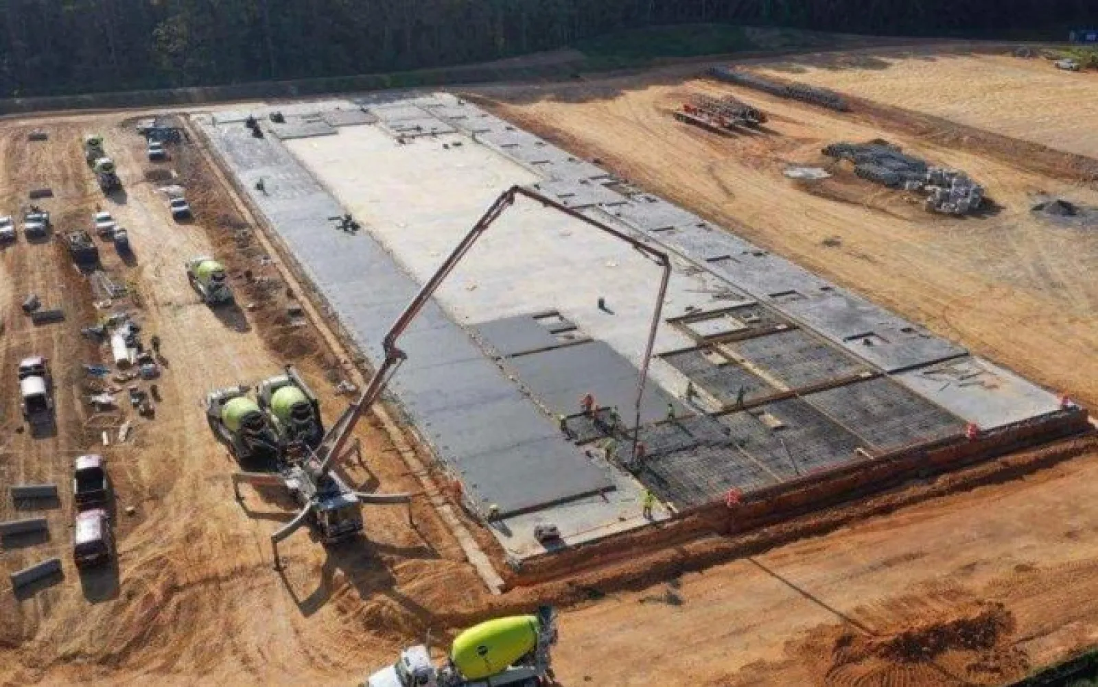 Aerial view of a large concrete slab foundation being poured at a construction site with multiple cement mixers.