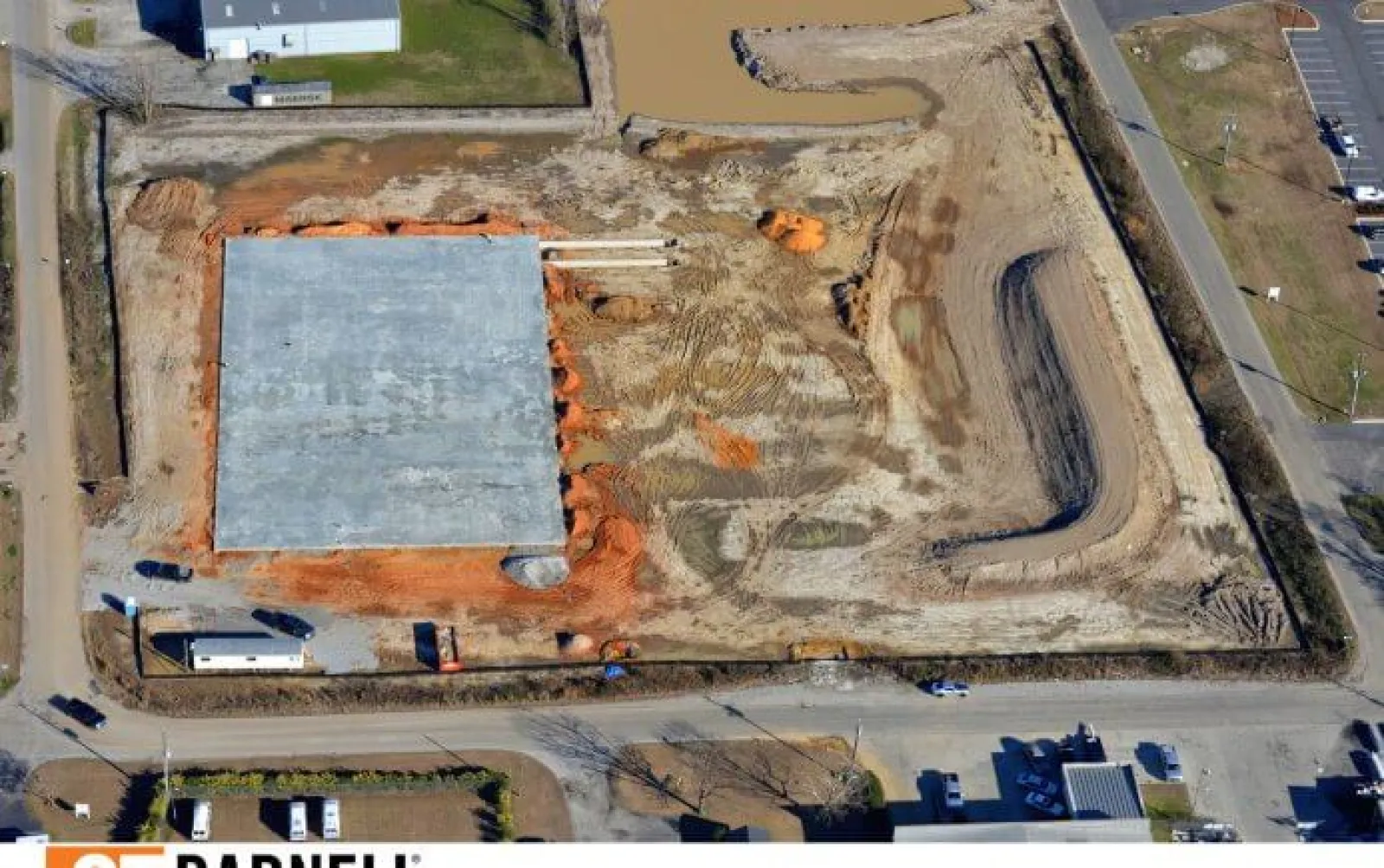 Aerial view of a construction site with concrete foundation and earthmoving activities in progress.
