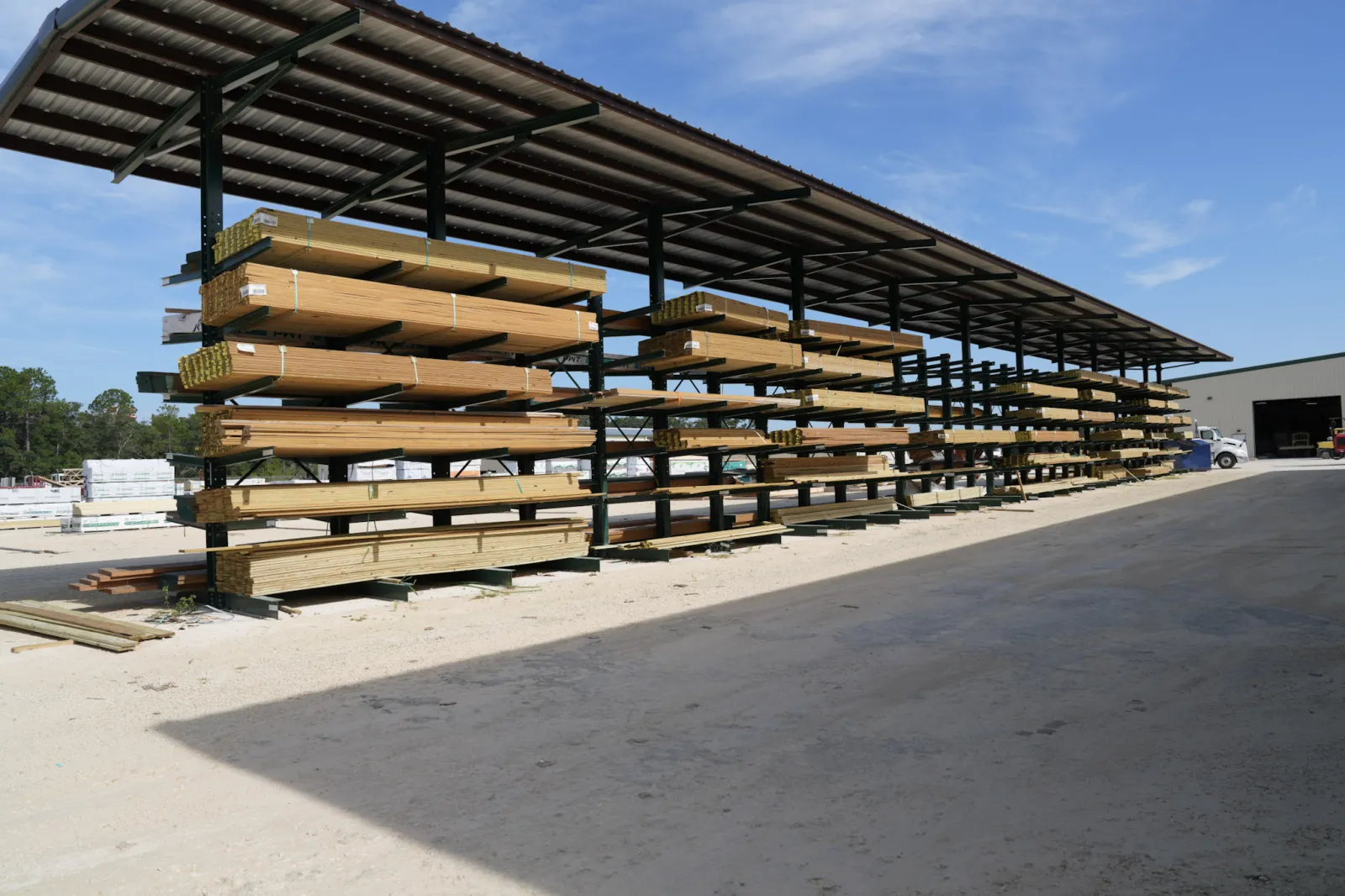 Outdoor lumber yard with stacked wooden planks under a metal canopy on a sunny day