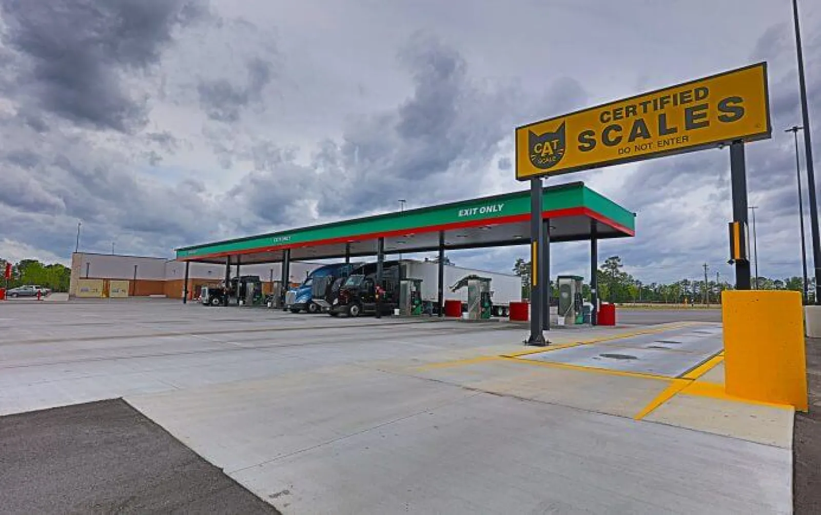 Truck stop with multiple fuel pumps under canopy and a large certified scales sign on a cloudy day