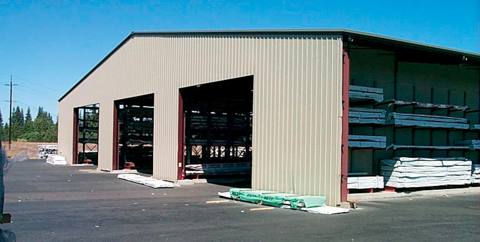 Large outdoor storage warehouse with metal siding storing lumber and construction materials on racks.