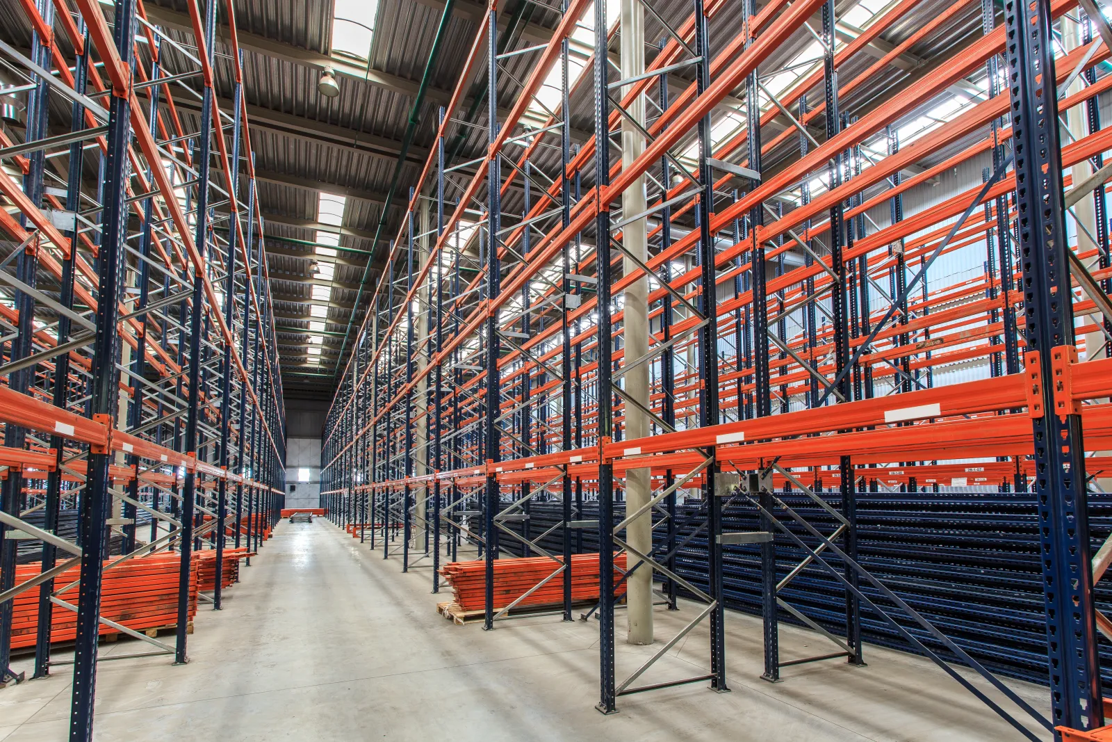 Empty industrial warehouse with tall metal storage racks and bright overhead lighting creating spacious aisles.