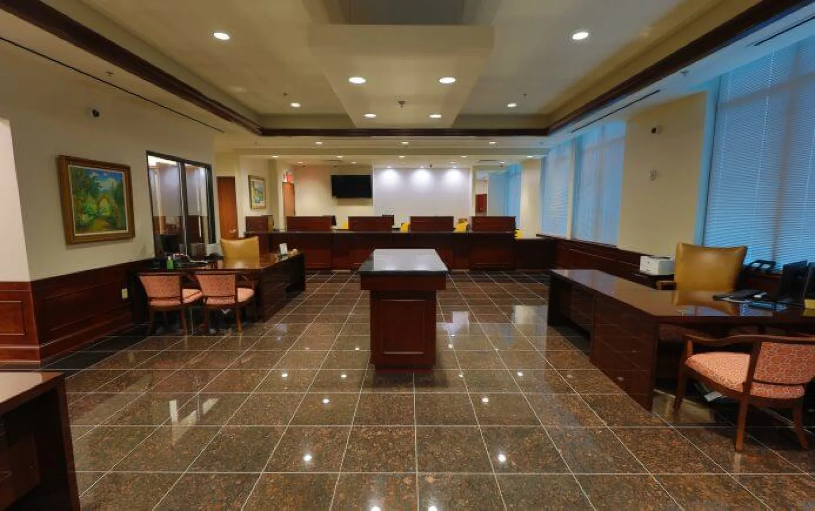 Spacious office lobby with glossy tiled floor, wooden desks, chairs, large windows, and subdued lighting.