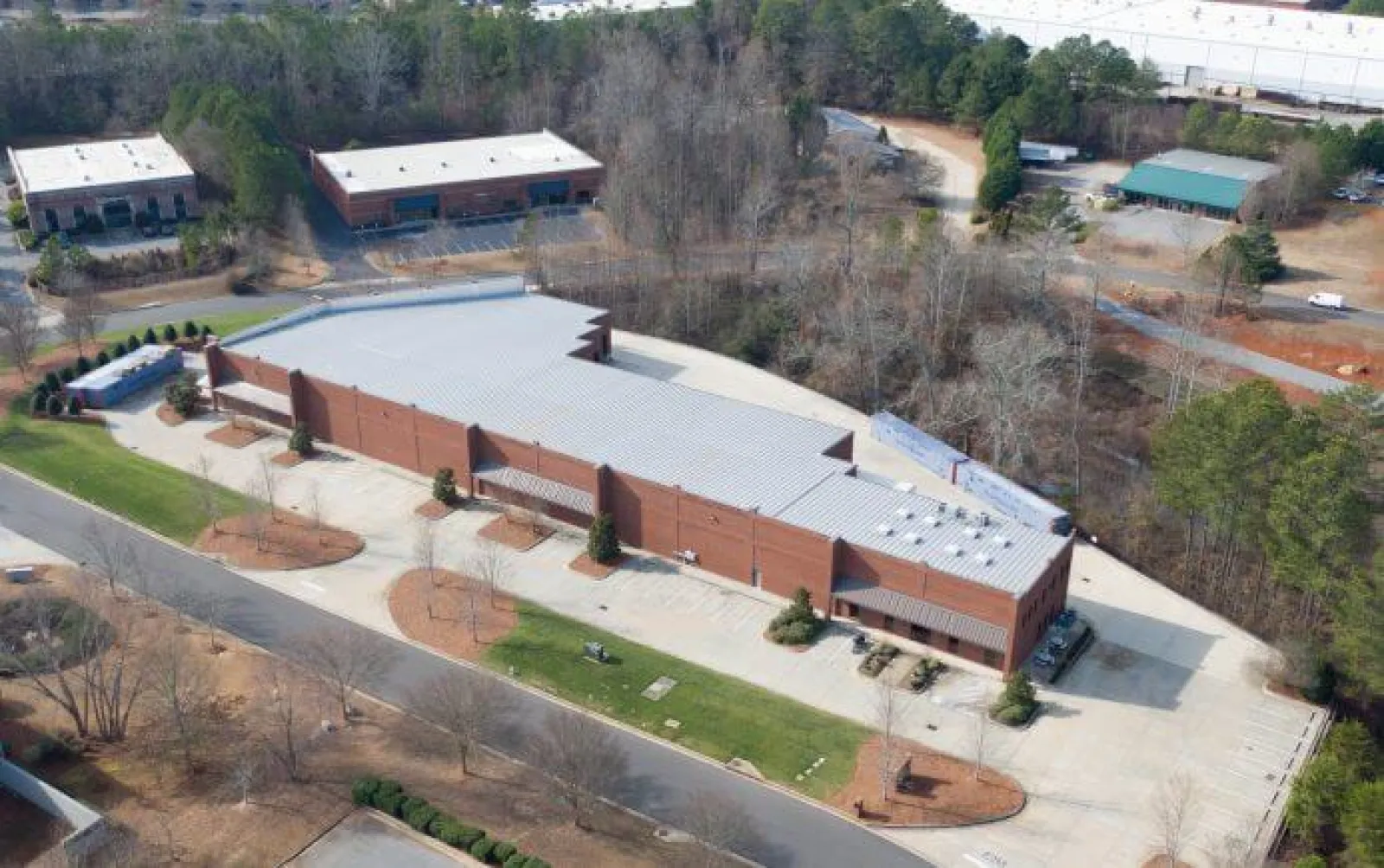 Aerial view of a large brick commercial building with a metal roof surrounded by trees and parking areas.