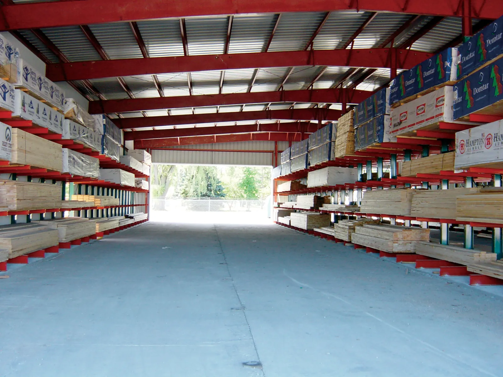 Warehouse with organized shelves storing lumber and building materials under a red steel roof structure.