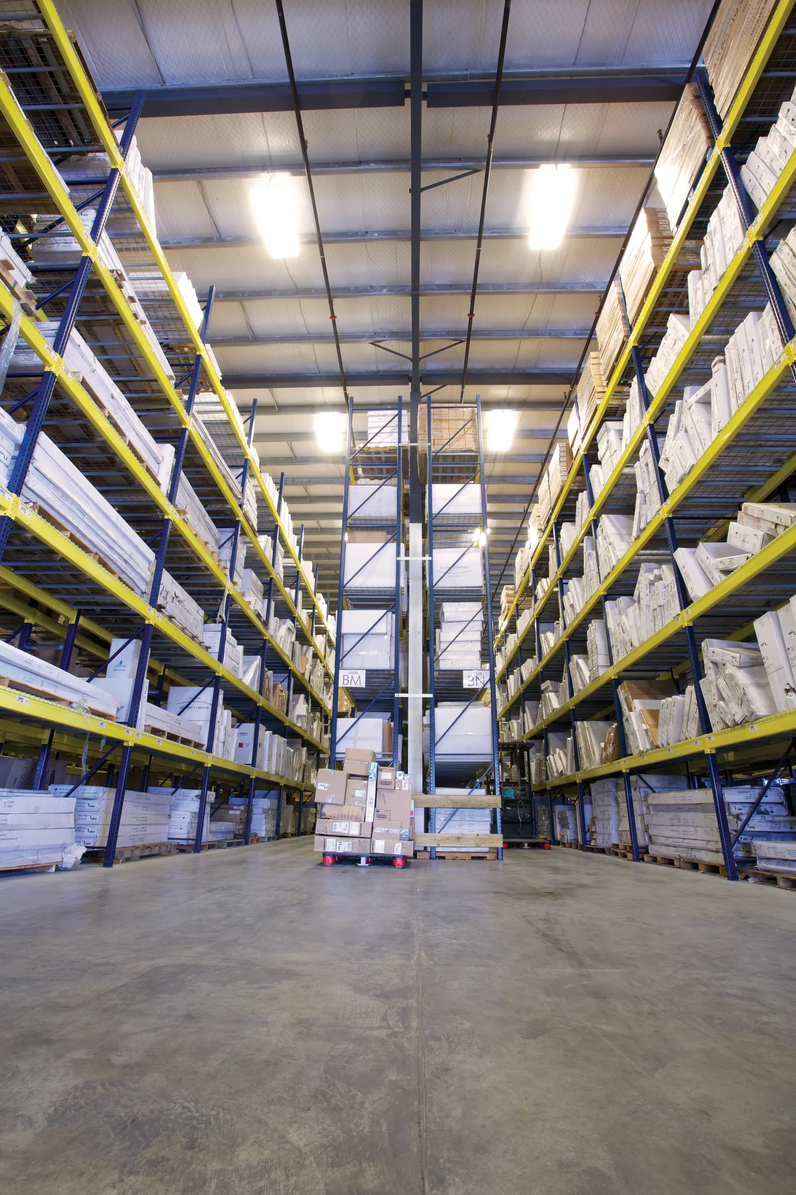 Interior of a large warehouse with tall shelves stocked with boxes and packages on a concrete floor.