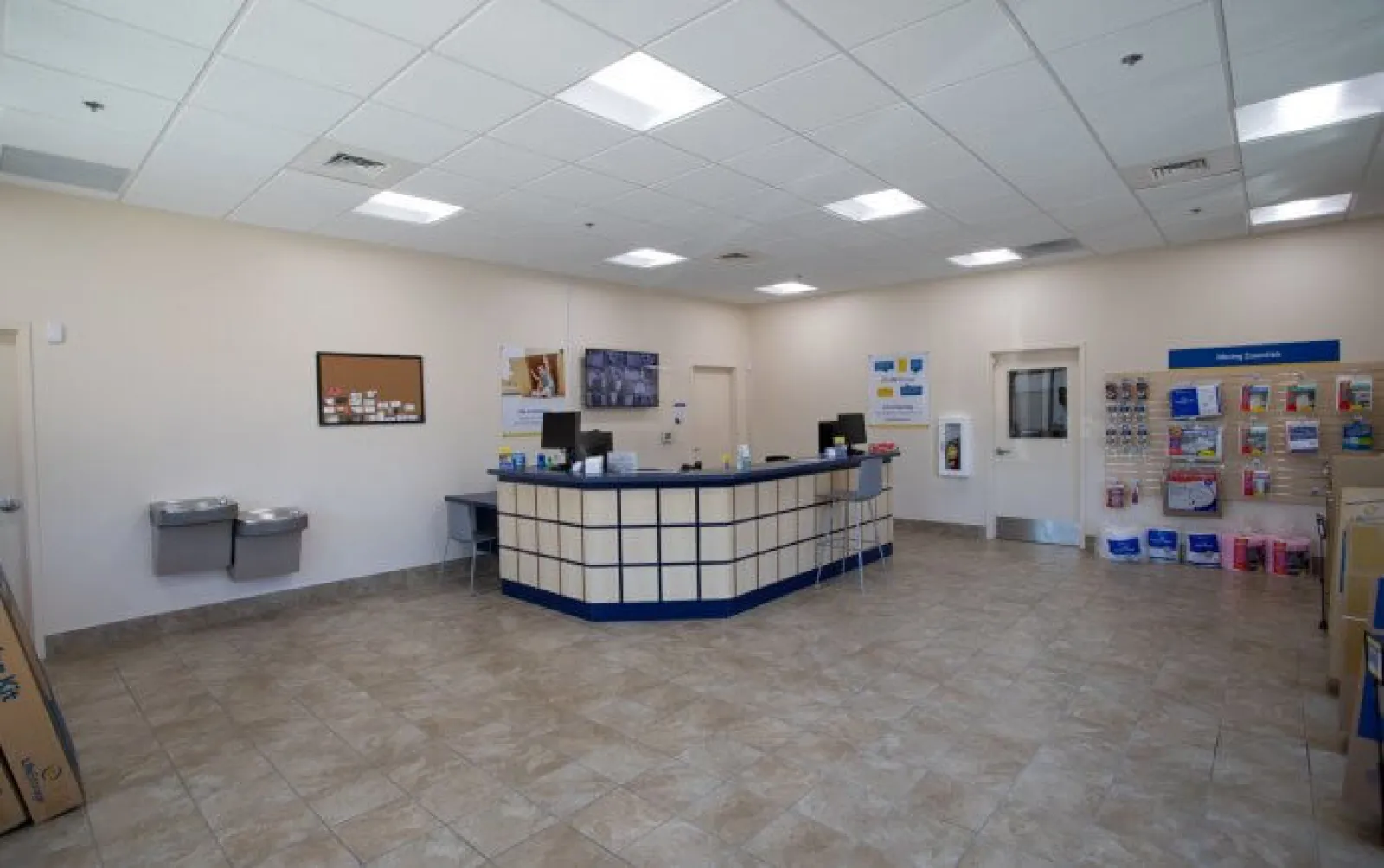 Clean postal service counter area with tiled floor, information display, and water fountains in a bright room.