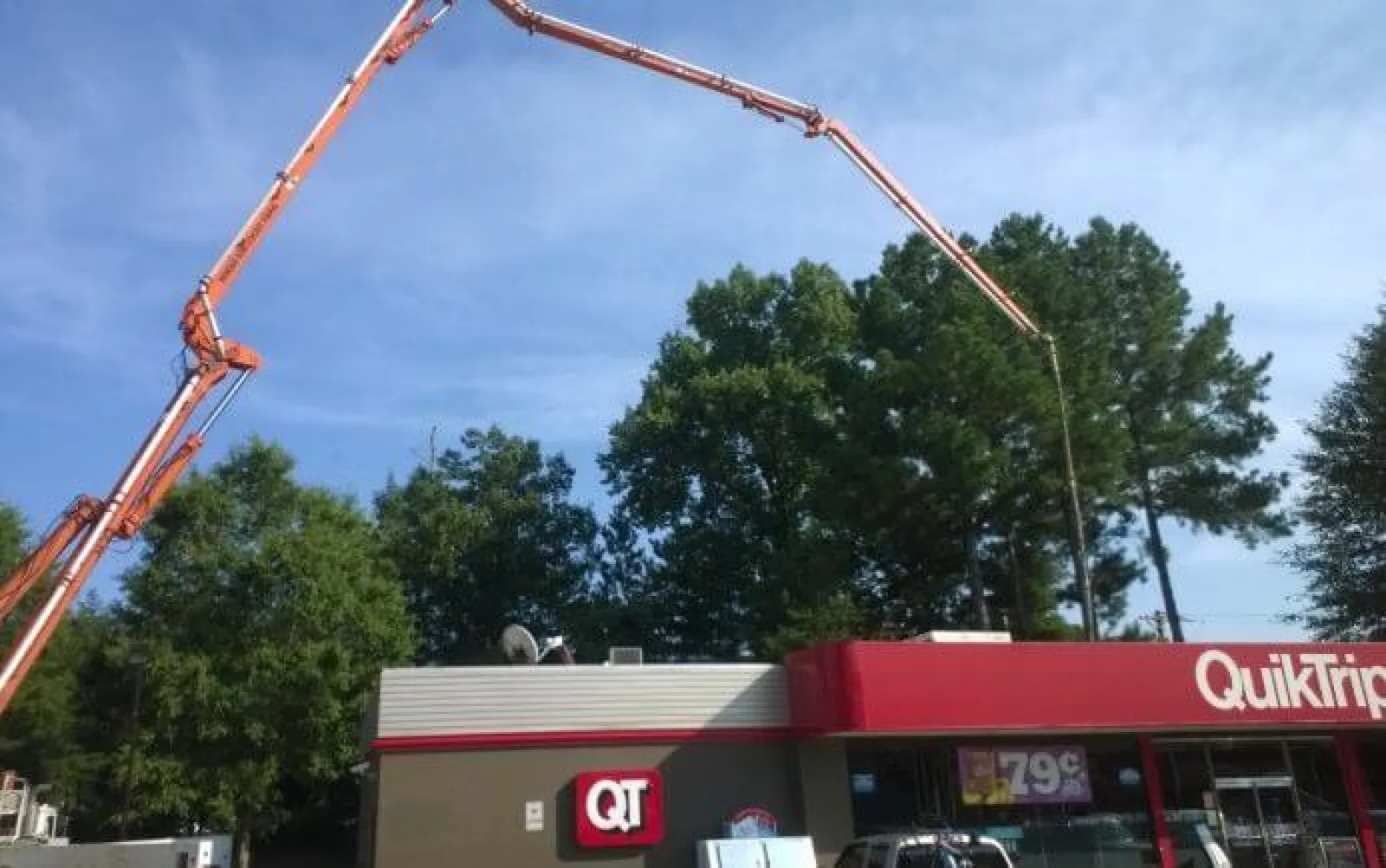 Concrete pump truck extending long arm over QuikTrip store with trees and blue sky in background