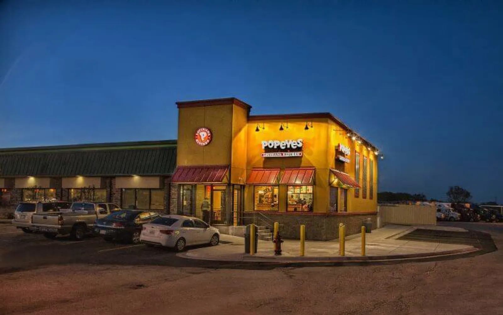 Popeyes Louisiana Kitchen restaurant lit up at night with cars parked outside in the parking lot.
